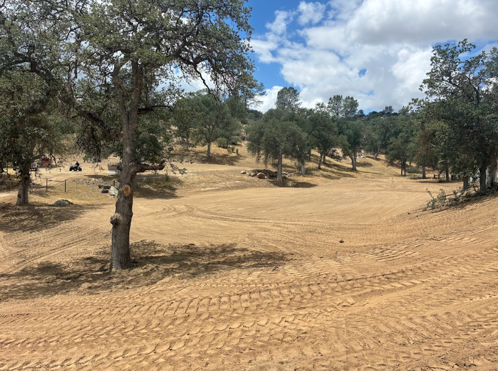 A dirt golf course fairway surrounded by trees under a partly cloudy sky.