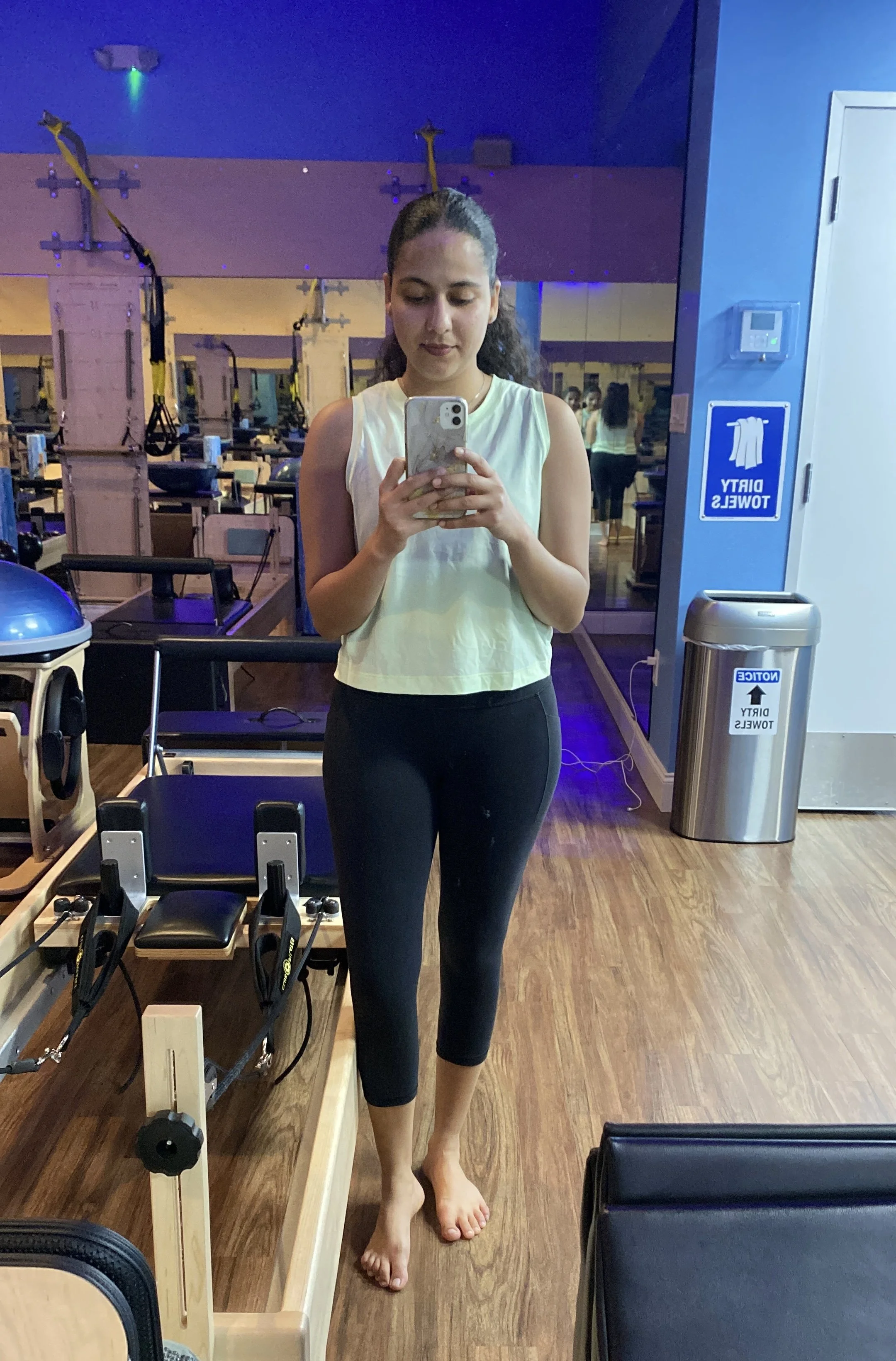 Akanksha Rathod, Founder of Nee's Physical Therapy Hoboken in a gym. The gym has fitness equipment and a mirror wall in the background.
