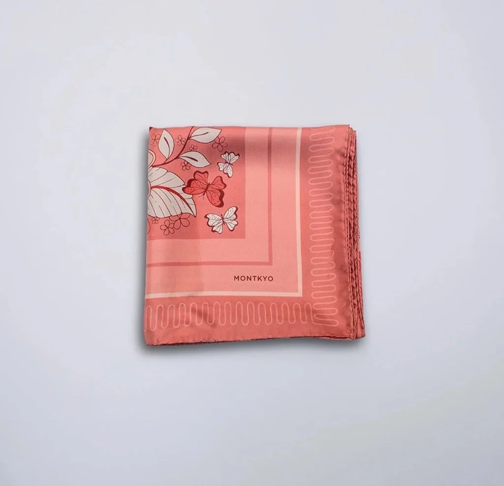 Wild Bloom silk scarf by MONTKYO folded into a square and laid flat on a white tabletop, showing part of the pattern.