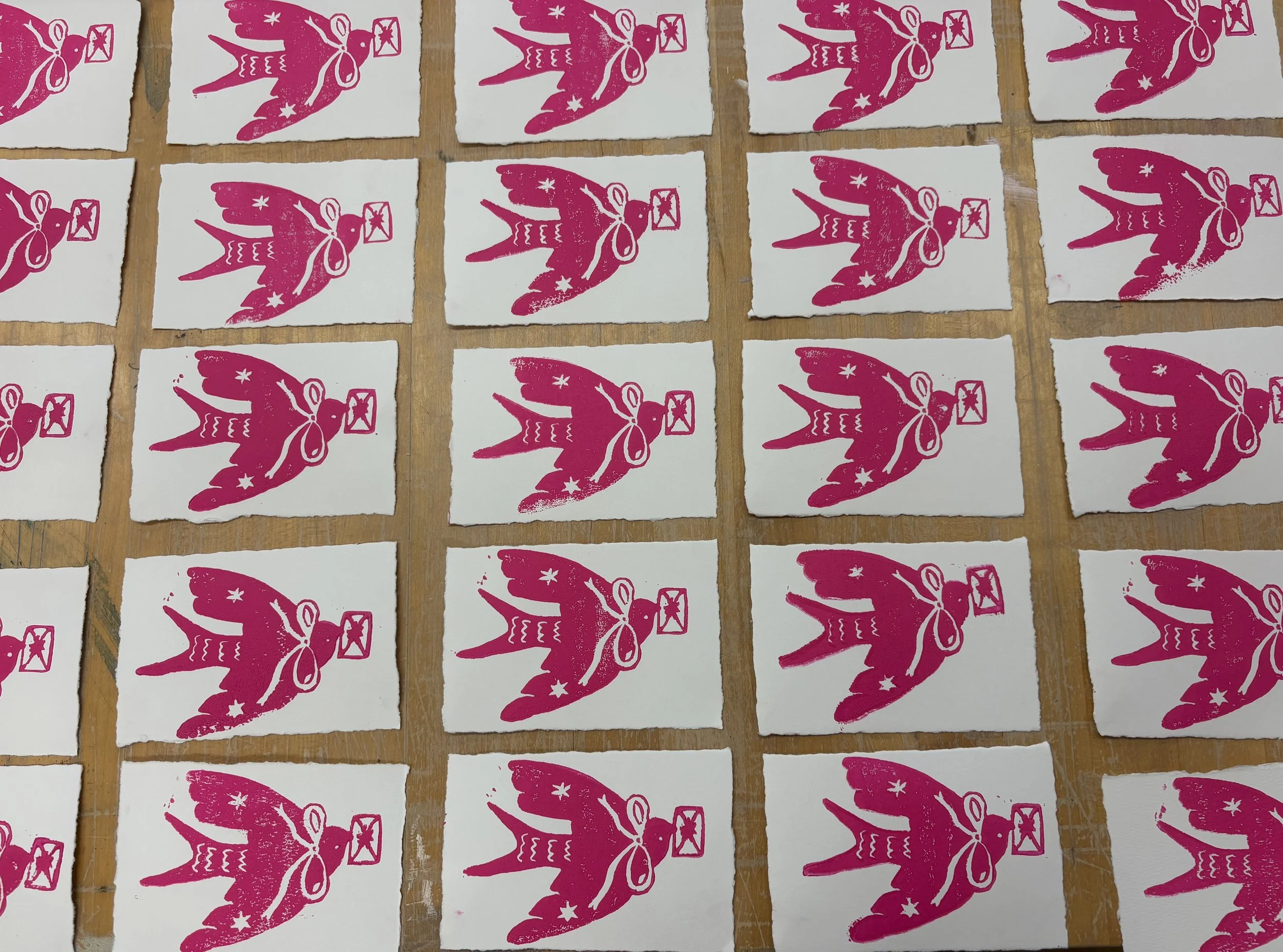 Multiple pink stamps of a rabbit holding an envelope, printed on small white paper cards arranged in grid on a wooden surface.
