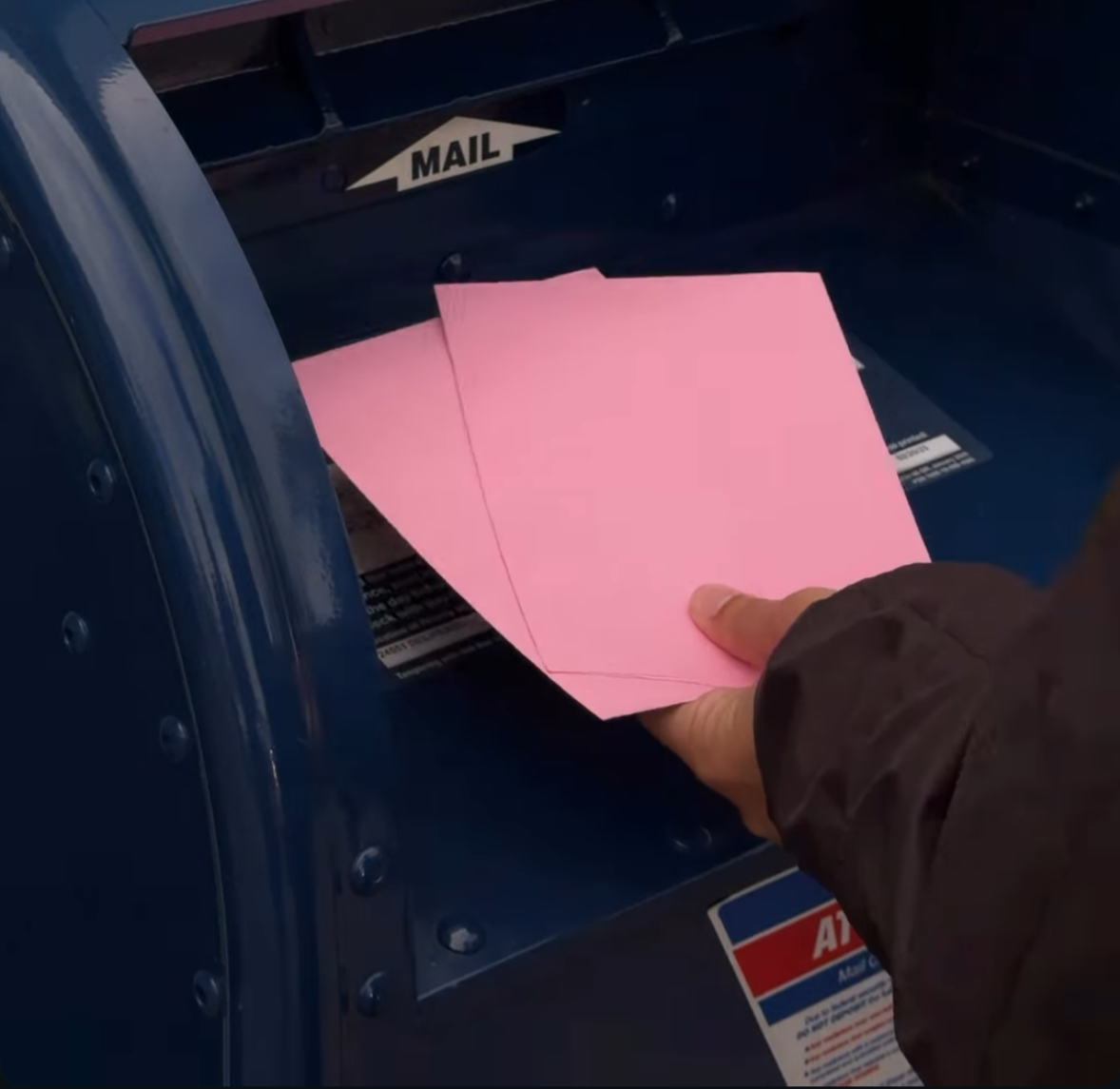 A person inserts pink mail envelopes into a blue mailbox labeled 'MAIL'.