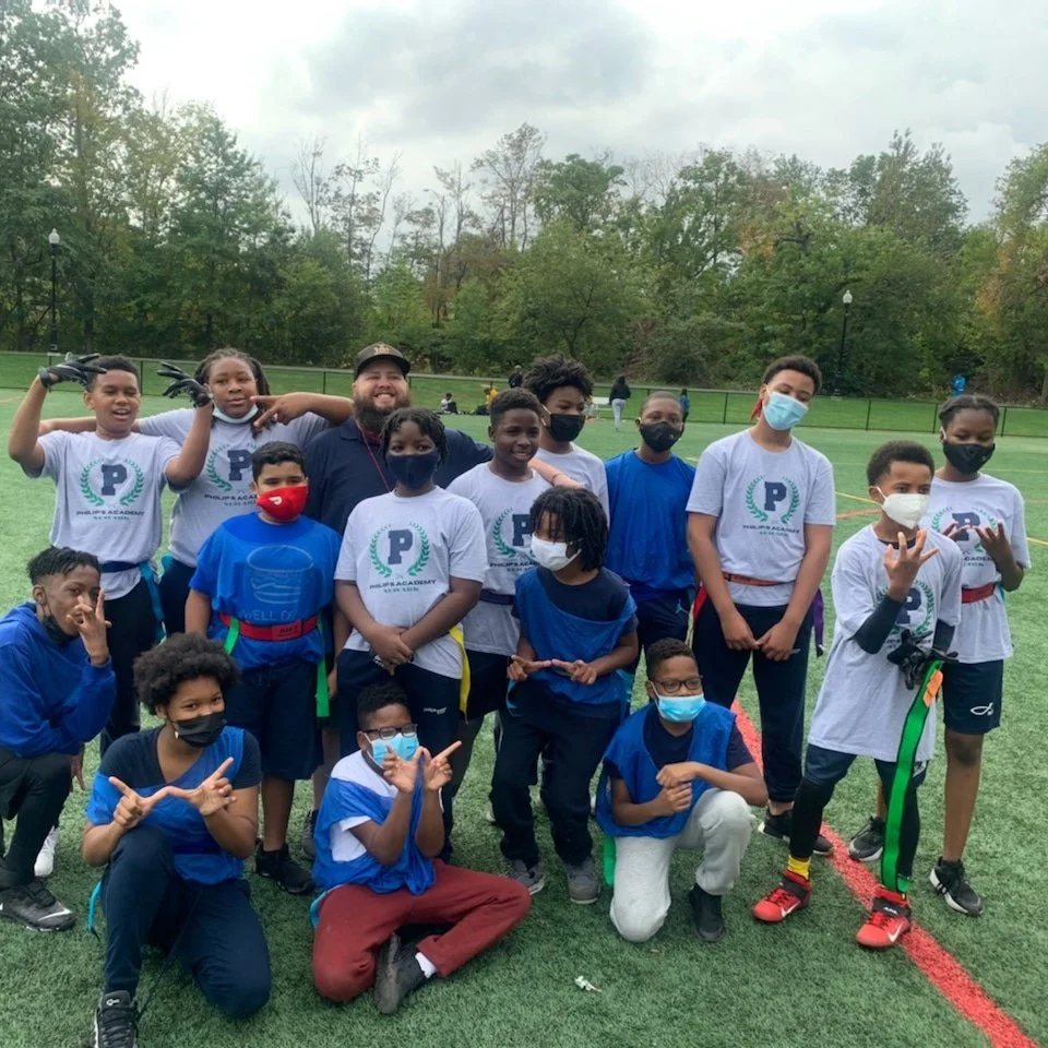 Group of children and a coach posing on a football field, some children wearing masks, children with medals and sports attire.