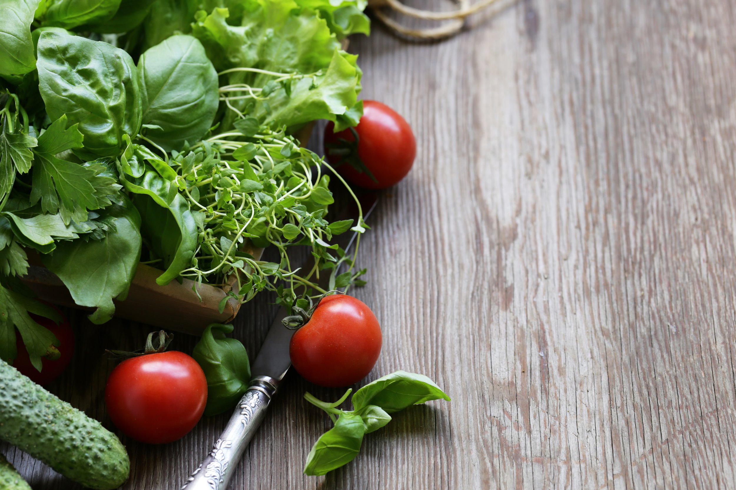 Fresh green leafy vegetables and ripe red tomatoes on a rustic wooden surface.
