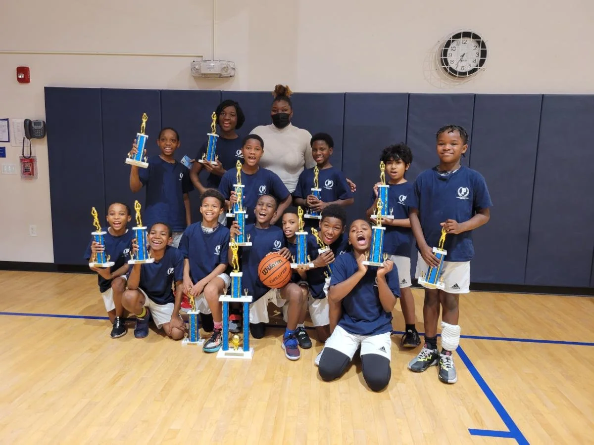 Youth basketball team with their coach in a gym, posing with trophies after a game or tournament.