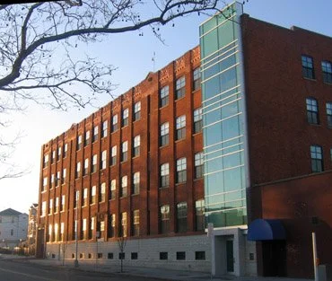 Red brick multi-story building with glass elevator shaft and blue awning.