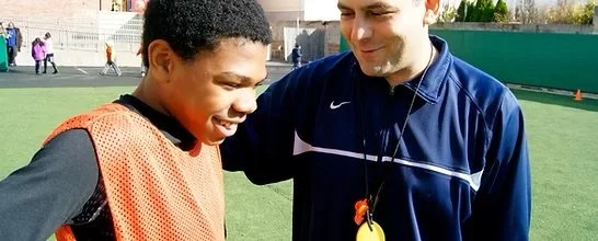 A coach talking to a young football player on a sports field.