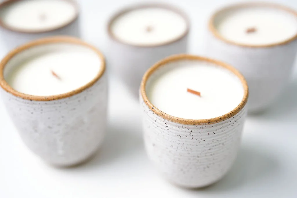 Several white candles in textured ceramic holders with unburned wicks, arranged on a white surface.