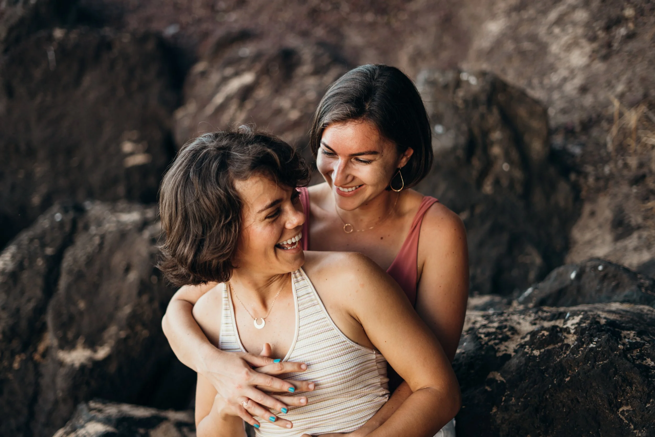 A same-sex LGBTQ+ couple shares a playful surf moment in open water. The scene emphasizes candid interaction and emotional authenticity. This Colorado-based photographer documents queer elopements across mountain and destination environments. The sty