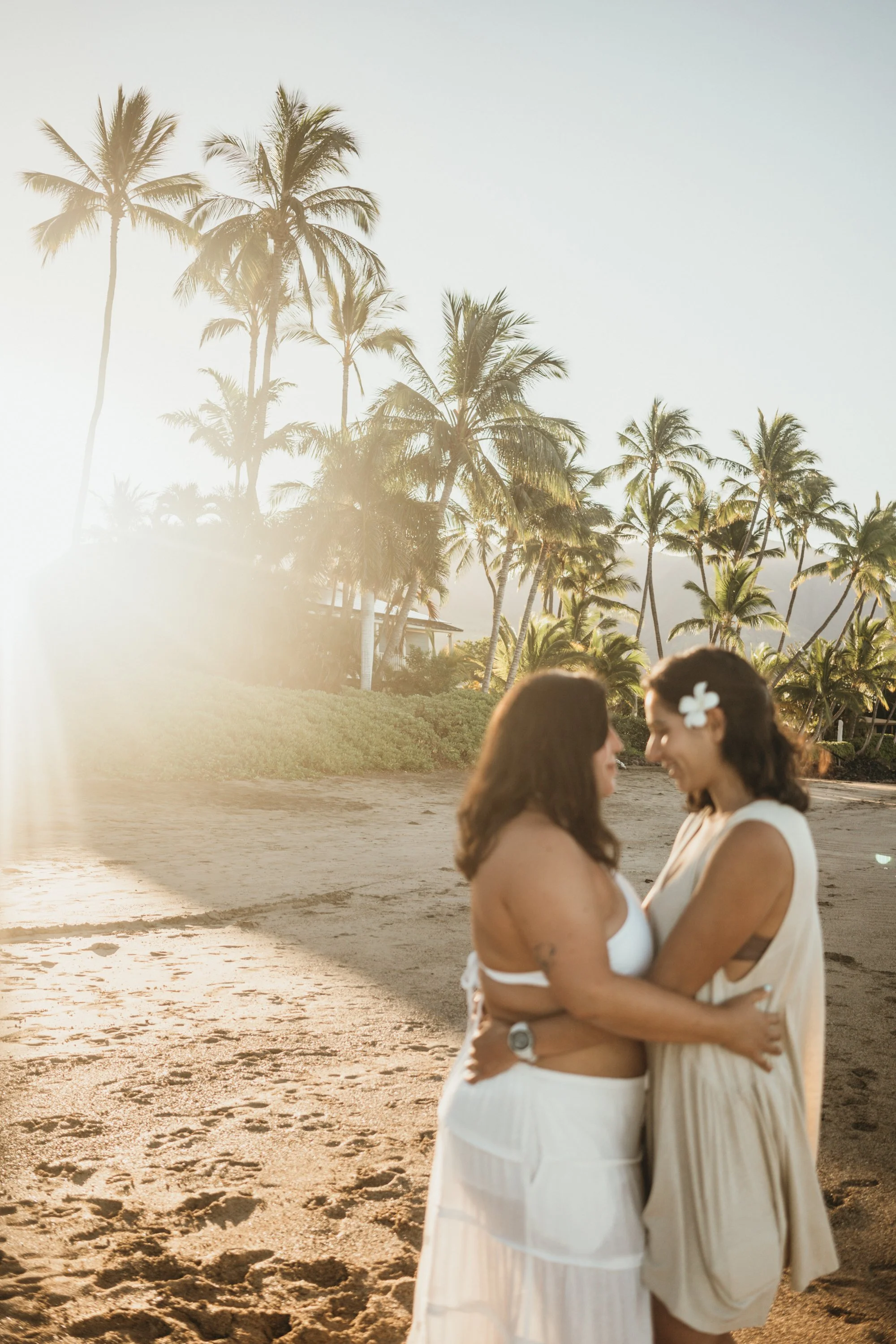 This engagement moment captures two women celebrating a sunrise proposal on the shoreline. The waves and sand create a soft and minimal natural backdrop. The photography style focuses on candid emotion rather than posed direction. While the location 