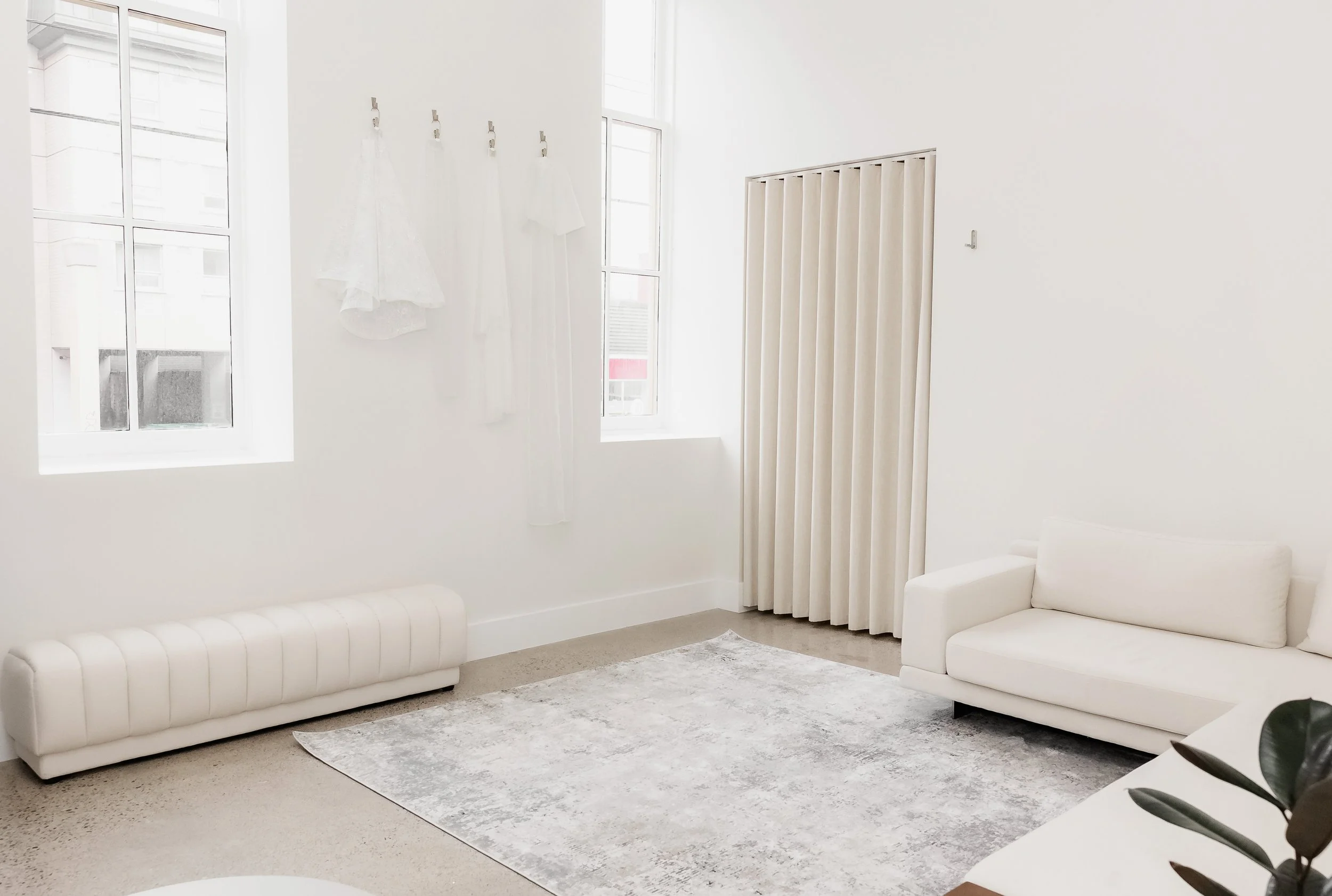 A bright, getting-ready space with white walls, two white sofas, large windows, and light-colored curtains.