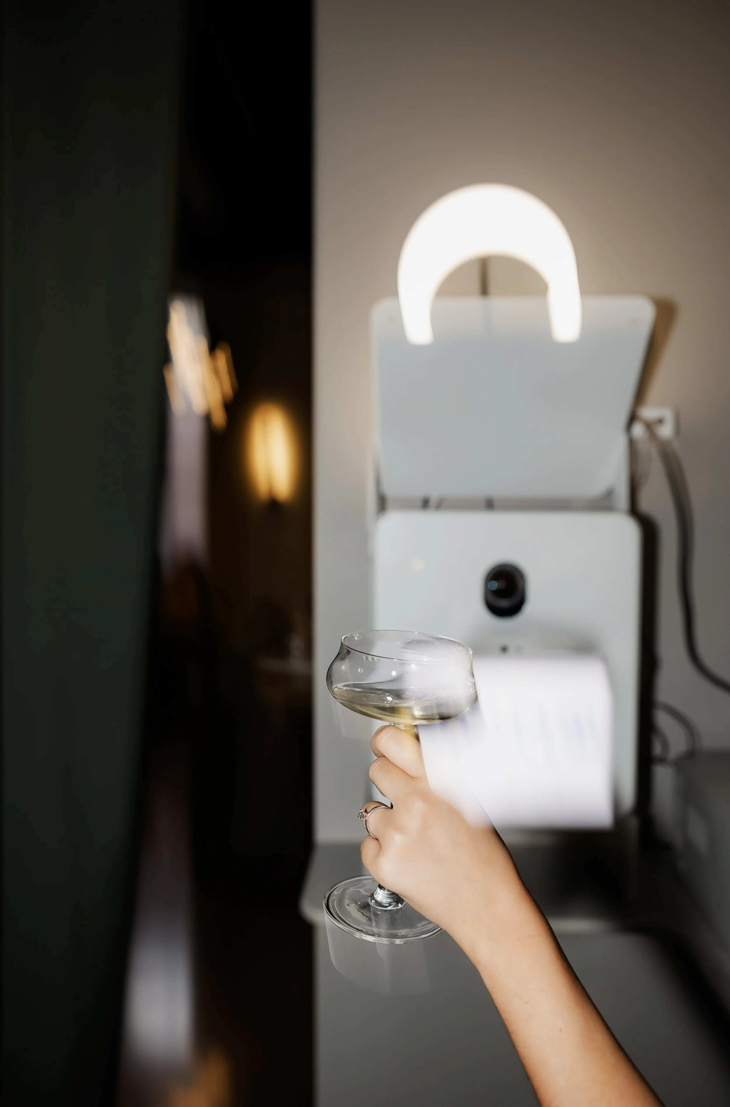 A person holding a glass of white wine in front of a white machine with a circular light on top, inside a dimly lit room.