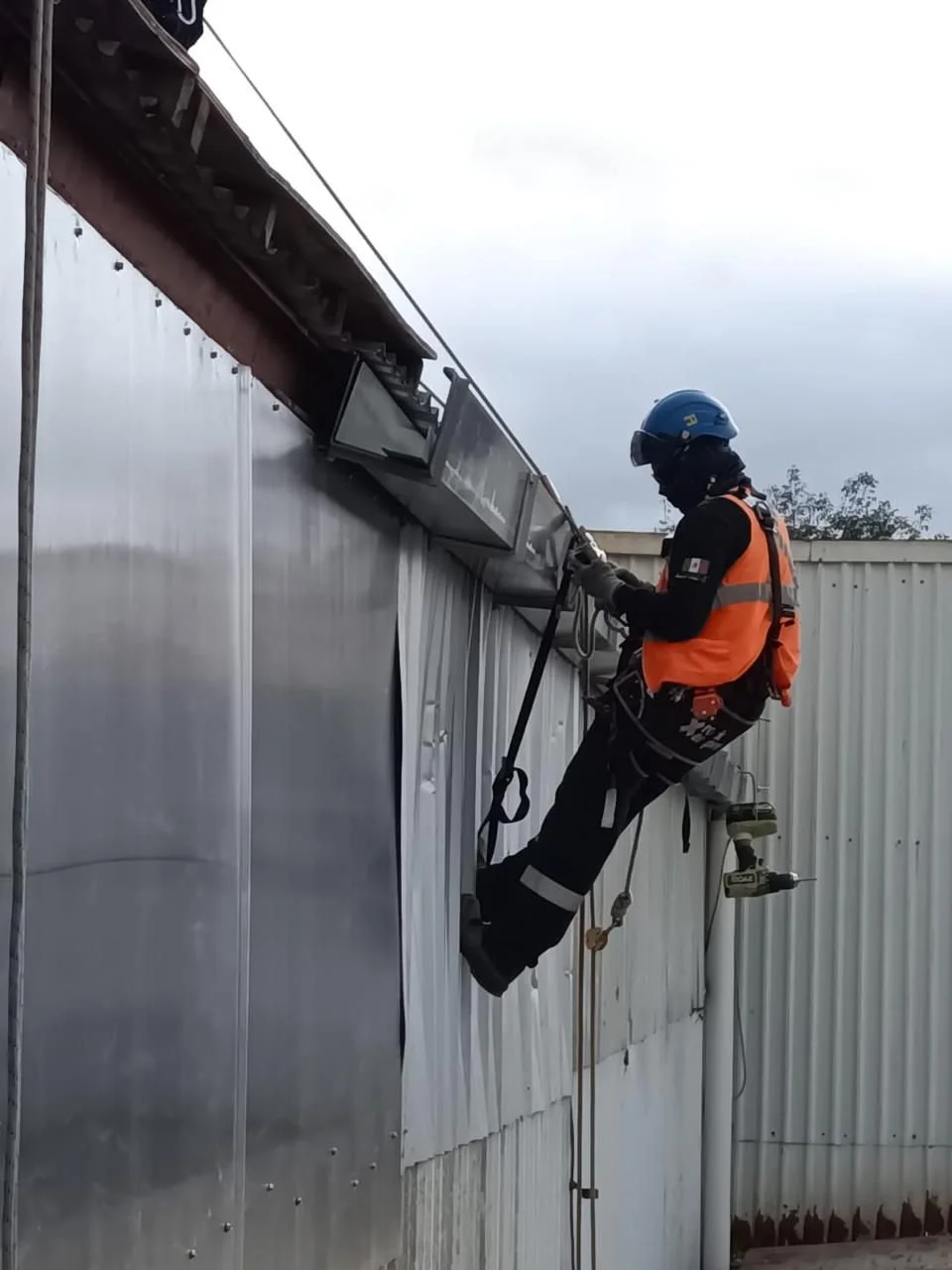 Trabajador en seguridad trabajando en la estructura exterior de un edificio de metal, con casco y arnés de seguridad.