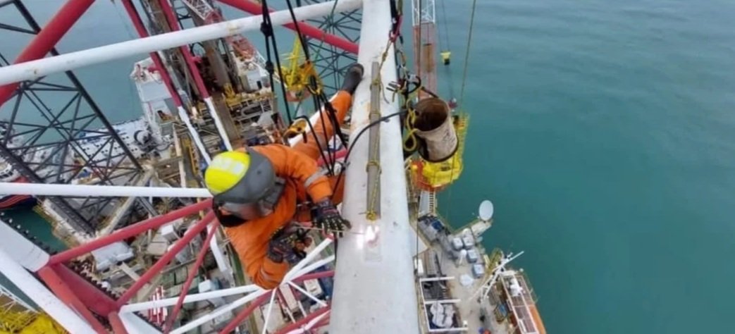 Trabajador en equipo realiza mantenimiento en estructura de torre de transmisión en alta mar.