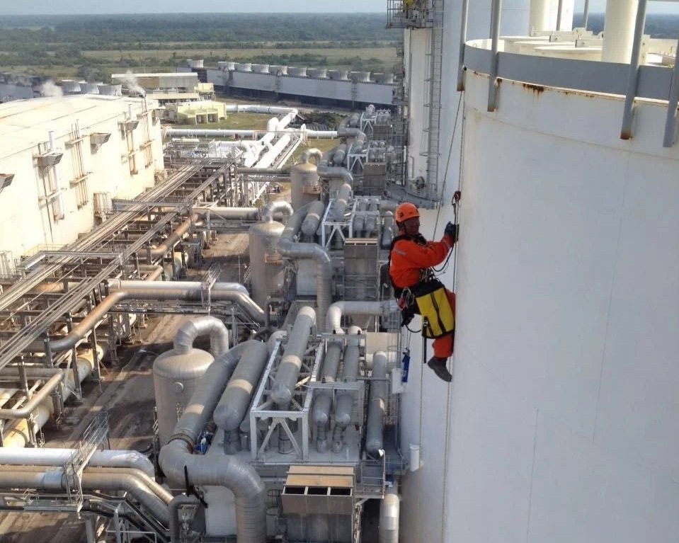 Trabajador en equipo de seguridad realizando mantenimiento en la estructura de una planta industrial desde una altura