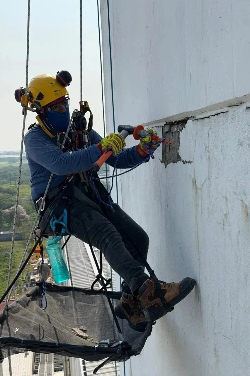 Trabajador en altura realizando mantenimiento en la pared de un edificio.