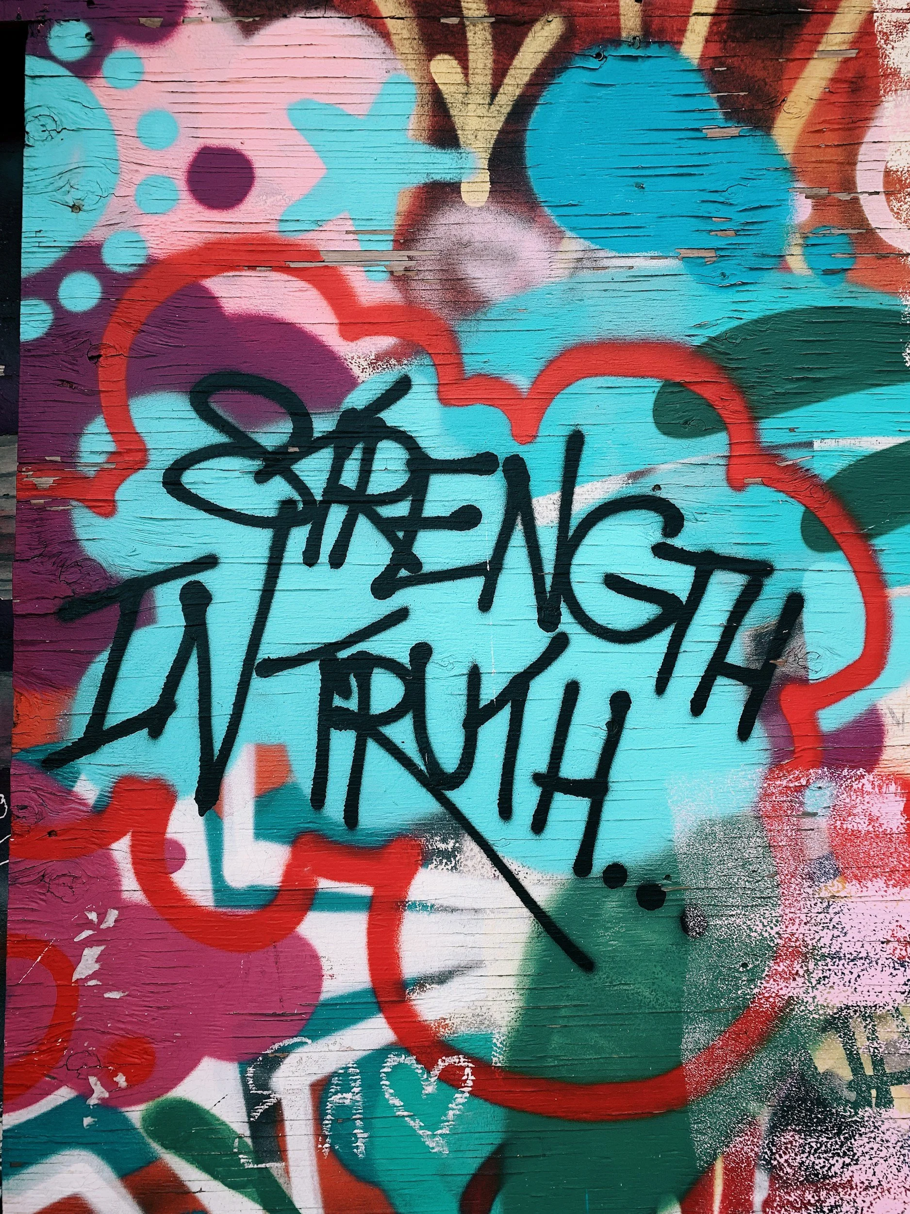 Colorful graffiti art on a wooden wall with various abstract shapes, dots, and spray paint, with the phrase "Strength in Truth" overlaid in black graffiti.
