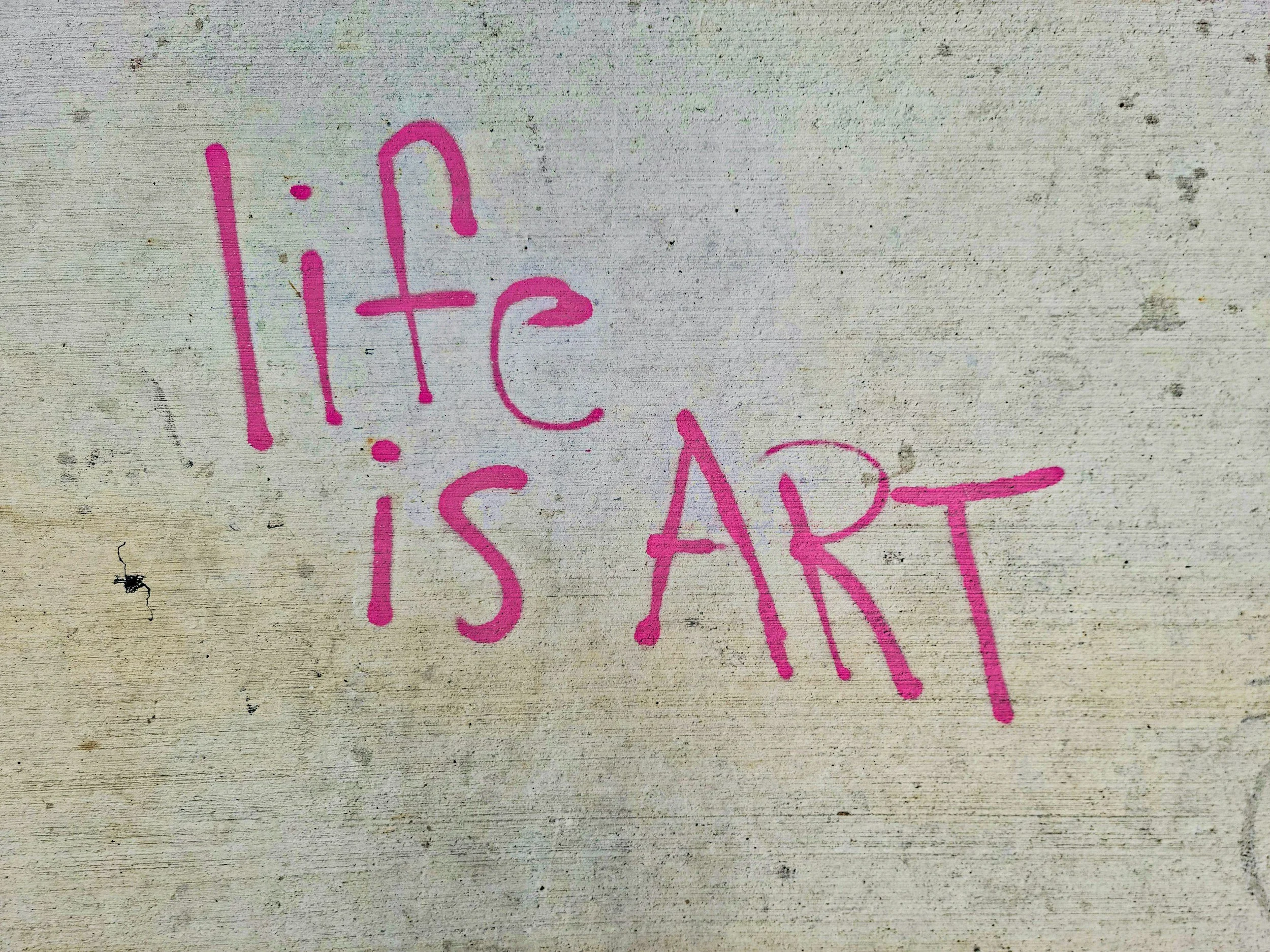 Pink graffiti on a weathered white wall that says "life is ART"