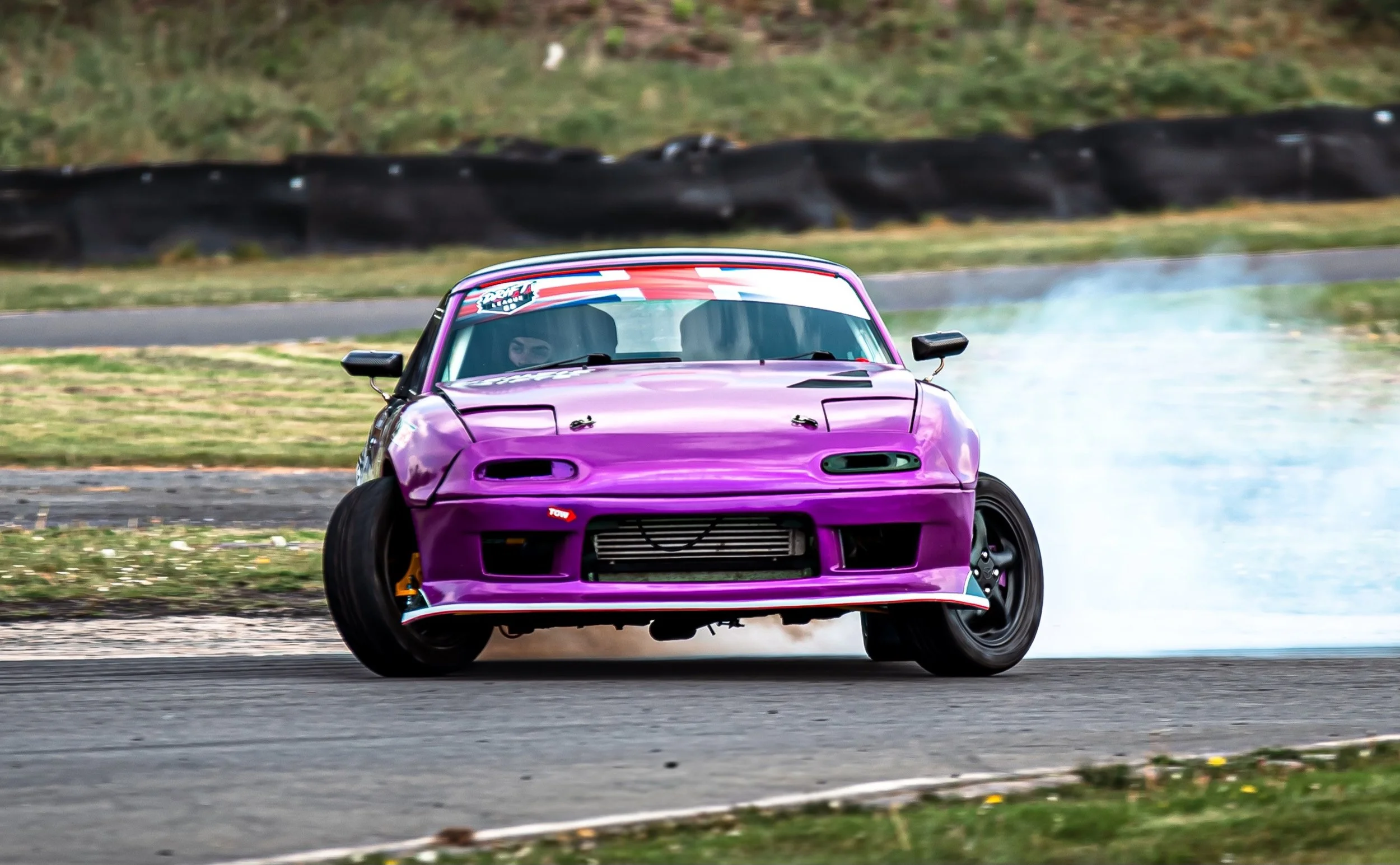 A purple sports car drifting on a racetrack, with smoke coming from the tires.