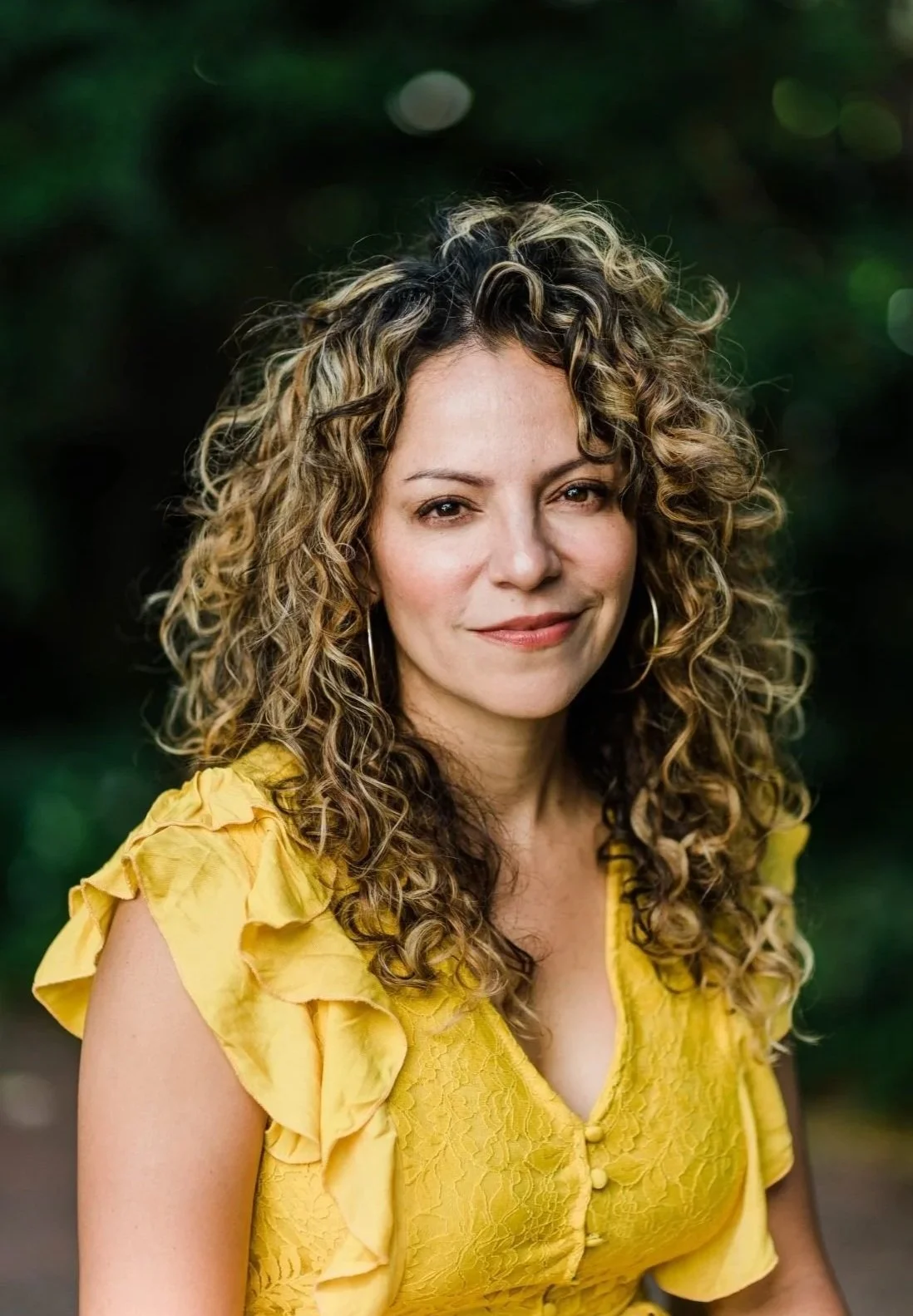 A woman with curly hair wearing a yellow dress outdoors.