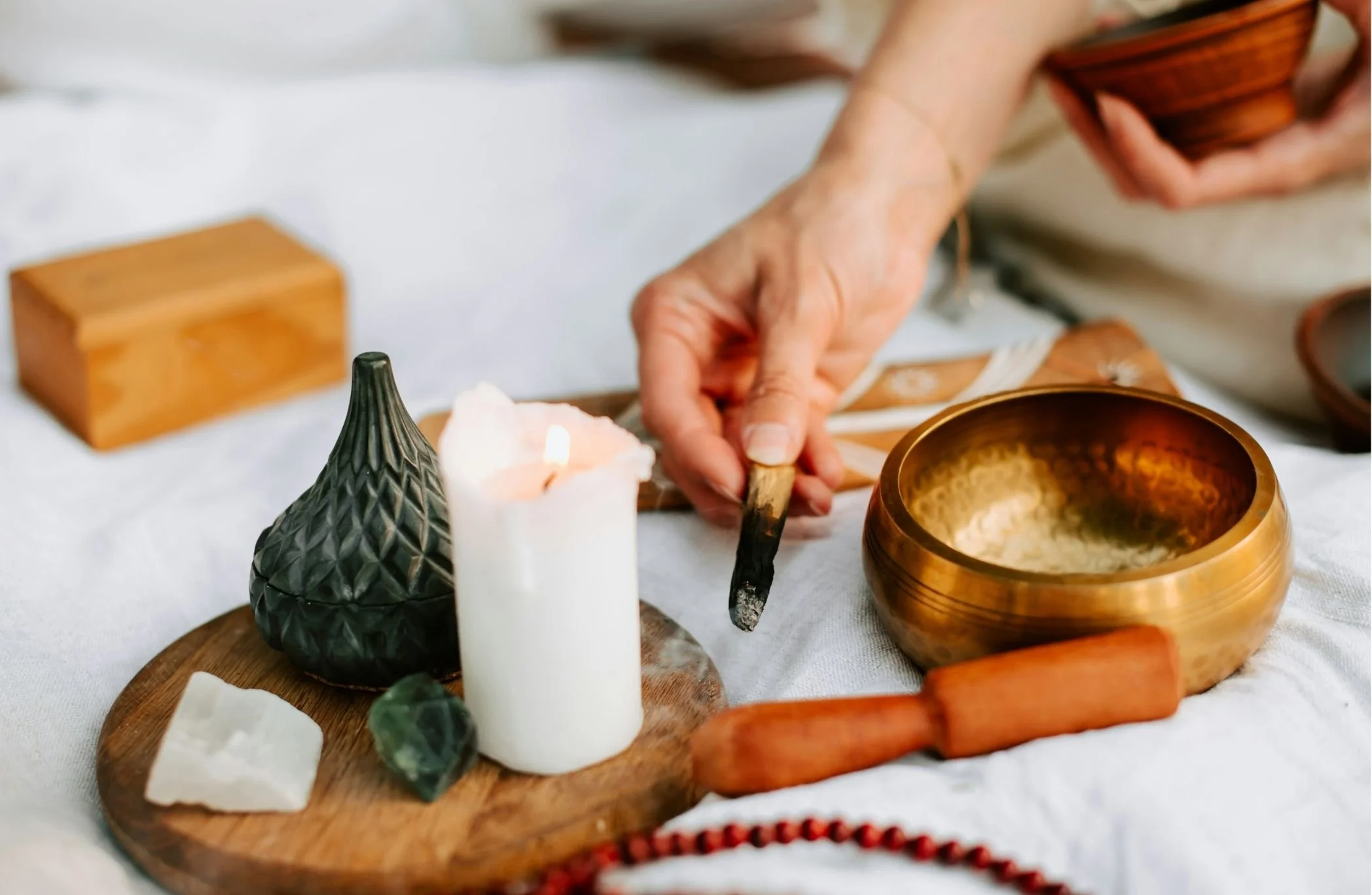 Person arranging decorative bowls and candles on a wooden tray, with a white candle and small green stones nearby.