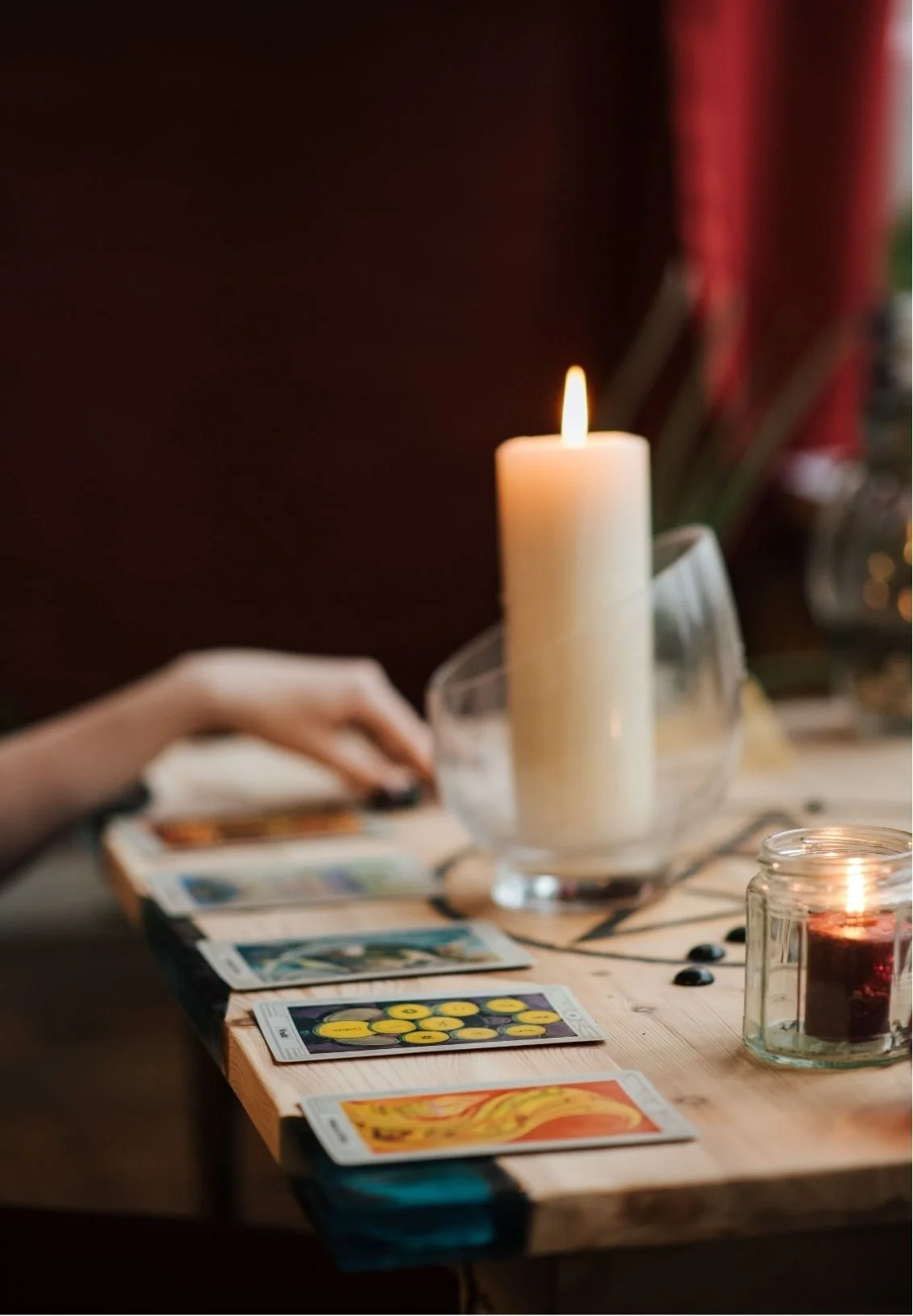 A table with tarot cards laid out, lit candles, and a hand reaching for one of the cards.