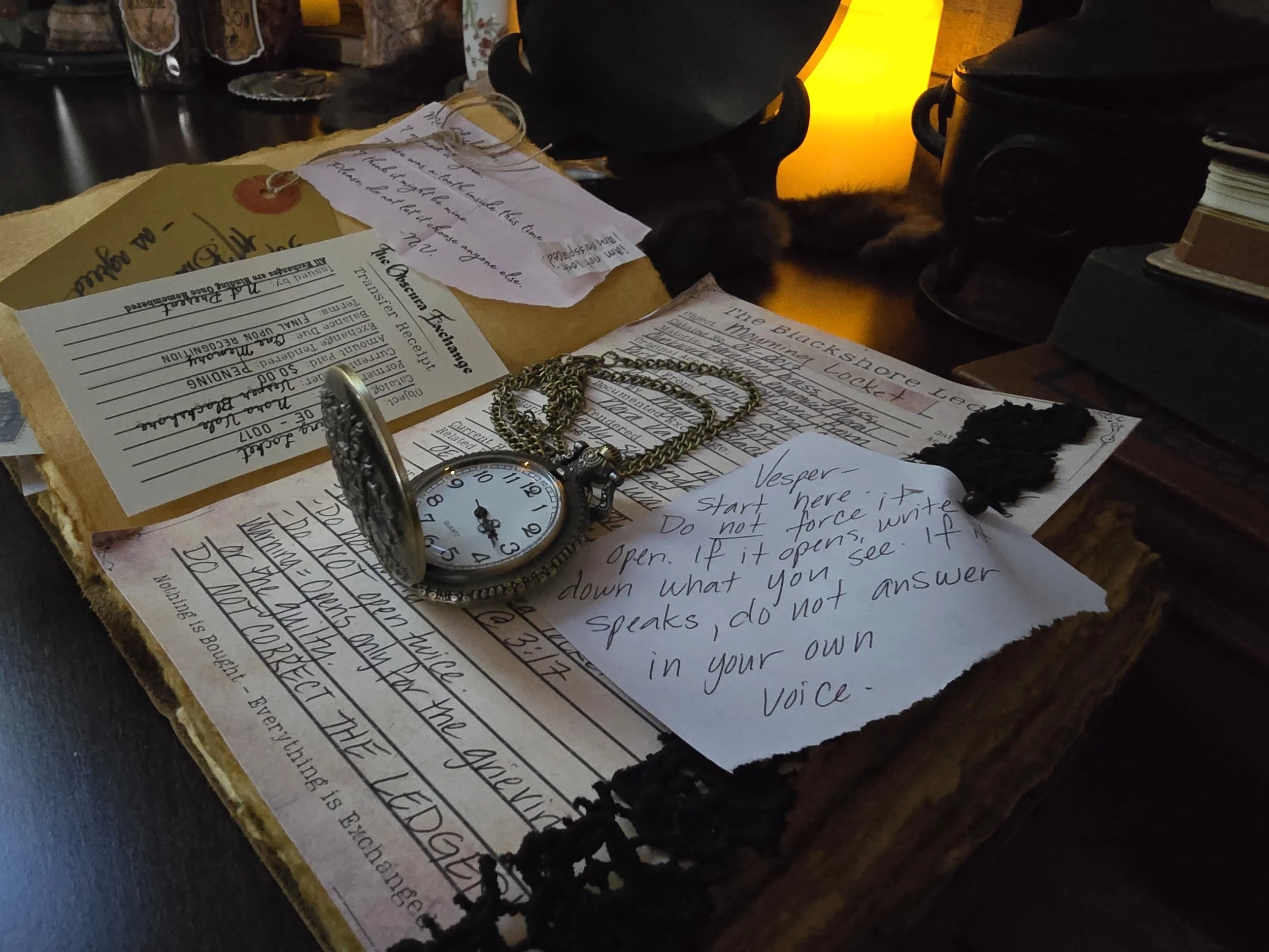 Various handwritten notes, jewelry, a pocket watch, and black yarn on a dark surface, possibly a desk or table, with some black containers and a yellow-lit object in the background.