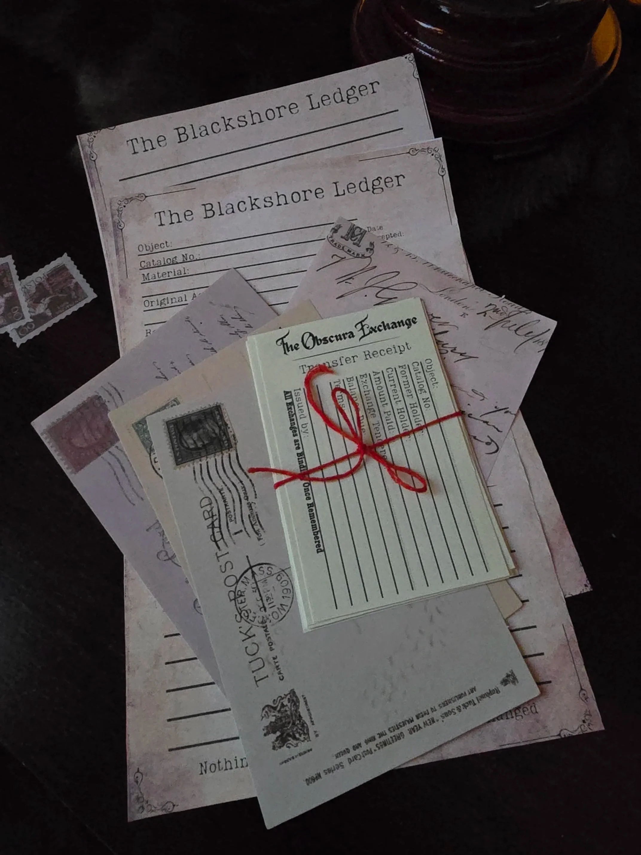 'The Blackshore Ledger' and 'The Oscura Exchange Transfer Receipt,' all held together with red string, on a dark surface.