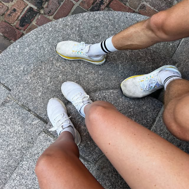 A photo taken from above of a man's legs next to a woman's legs wearing athletic sneakers on curved concrete steps. 