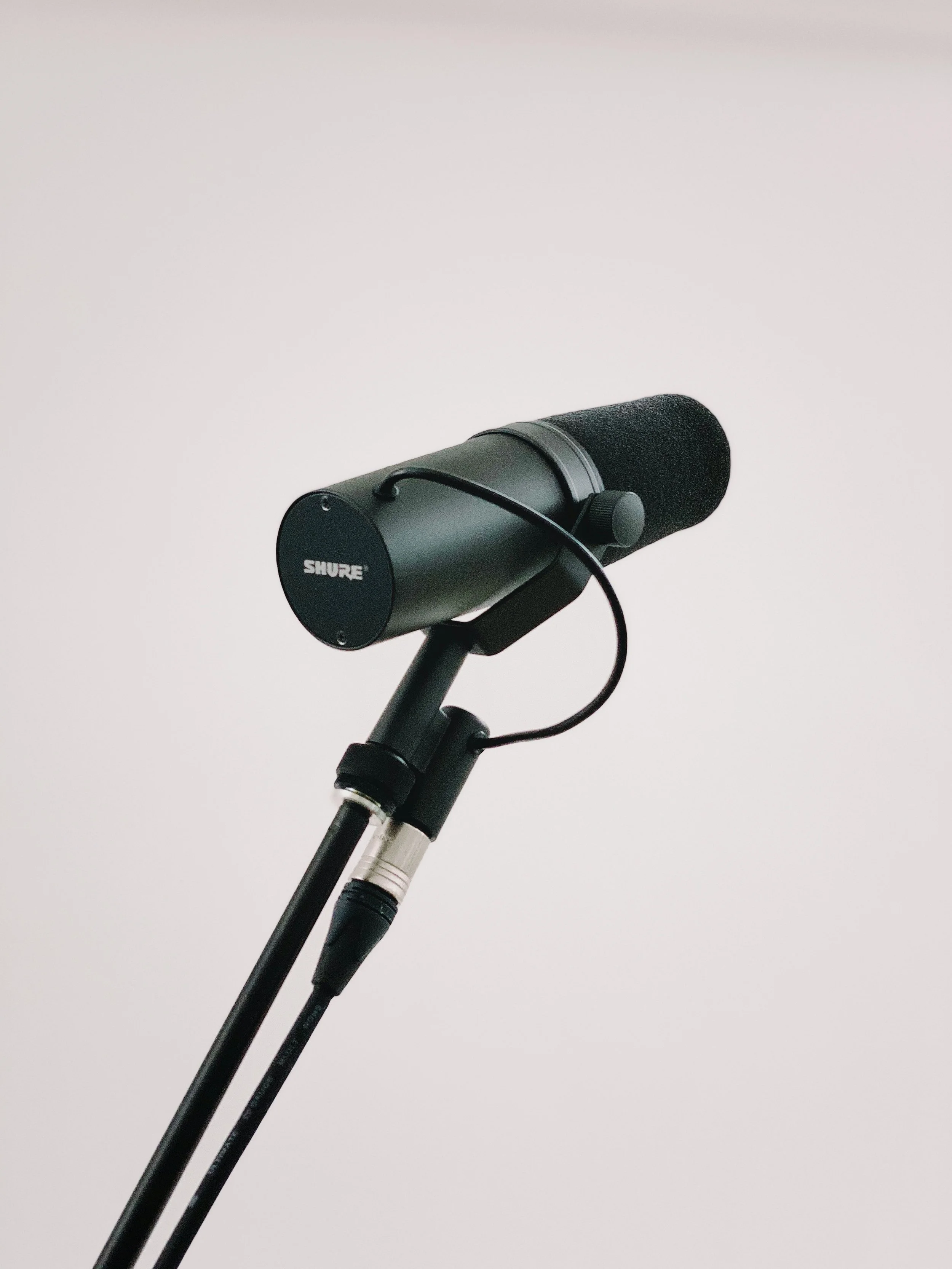 Close-up of a black Shure microphone mounted on a stand against a plain white background.