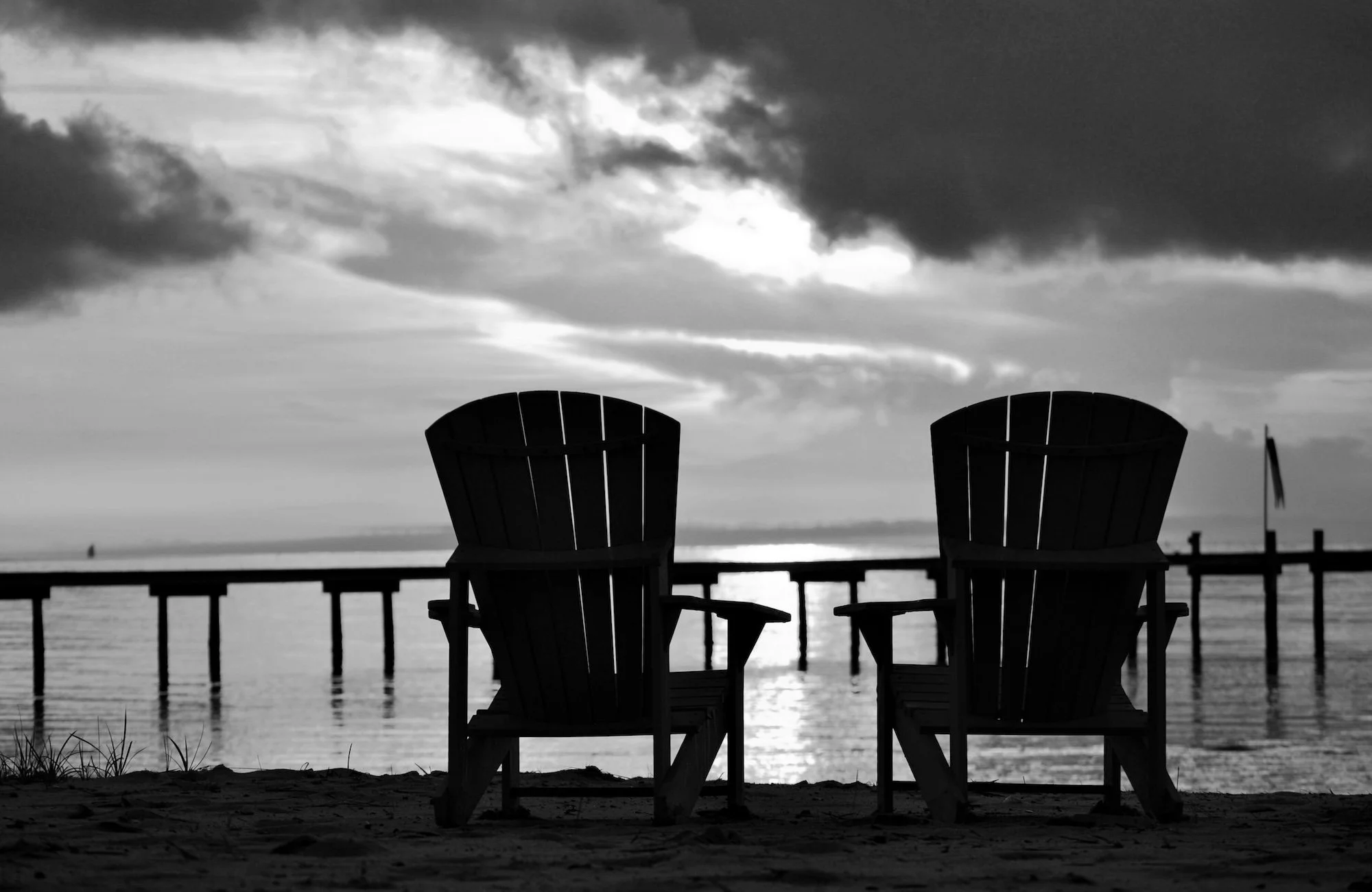 Two empty Adirondack chairs facing the water at sunset.