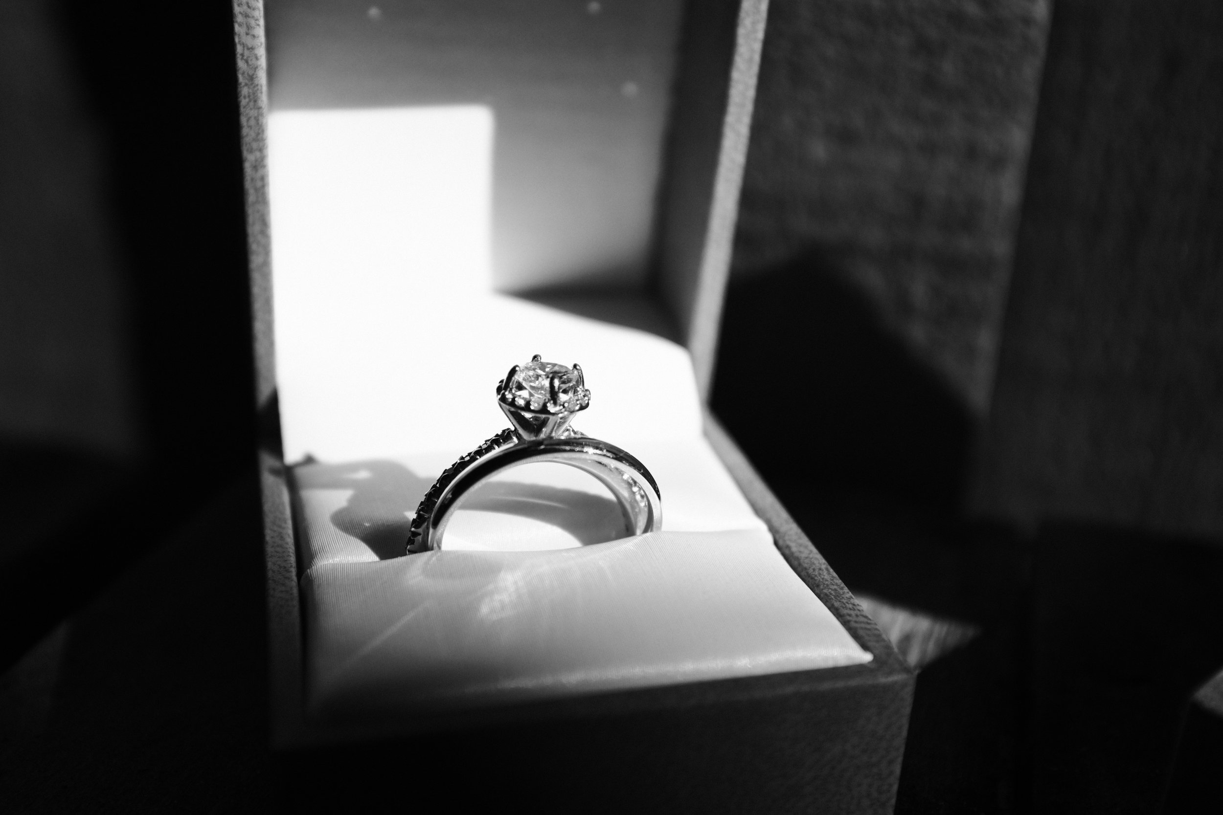 A diamond engagement ring in a jewelry box with a dark interior, with the ring having a large central diamond and smaller diamonds along the band.
