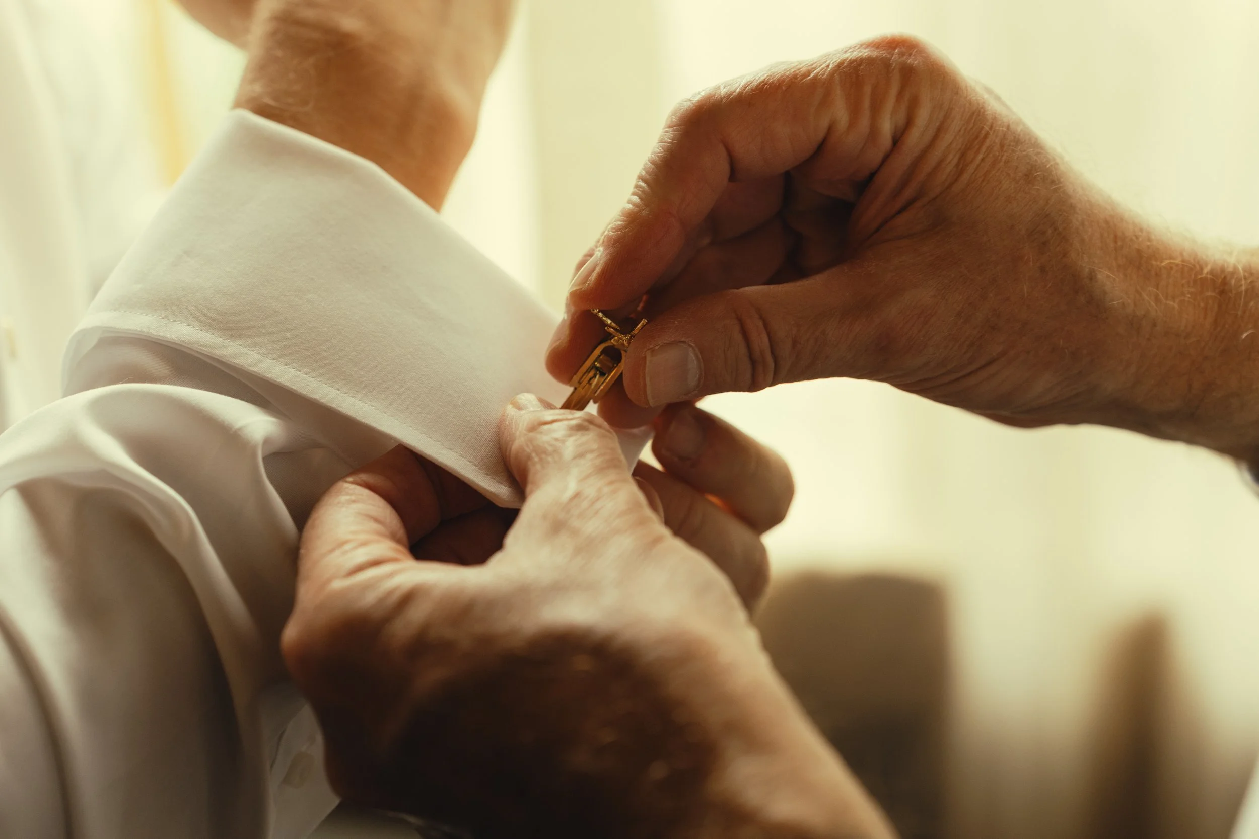 Close-up of elderly person's hand fastening a gold necklace around the back of a person's neck.