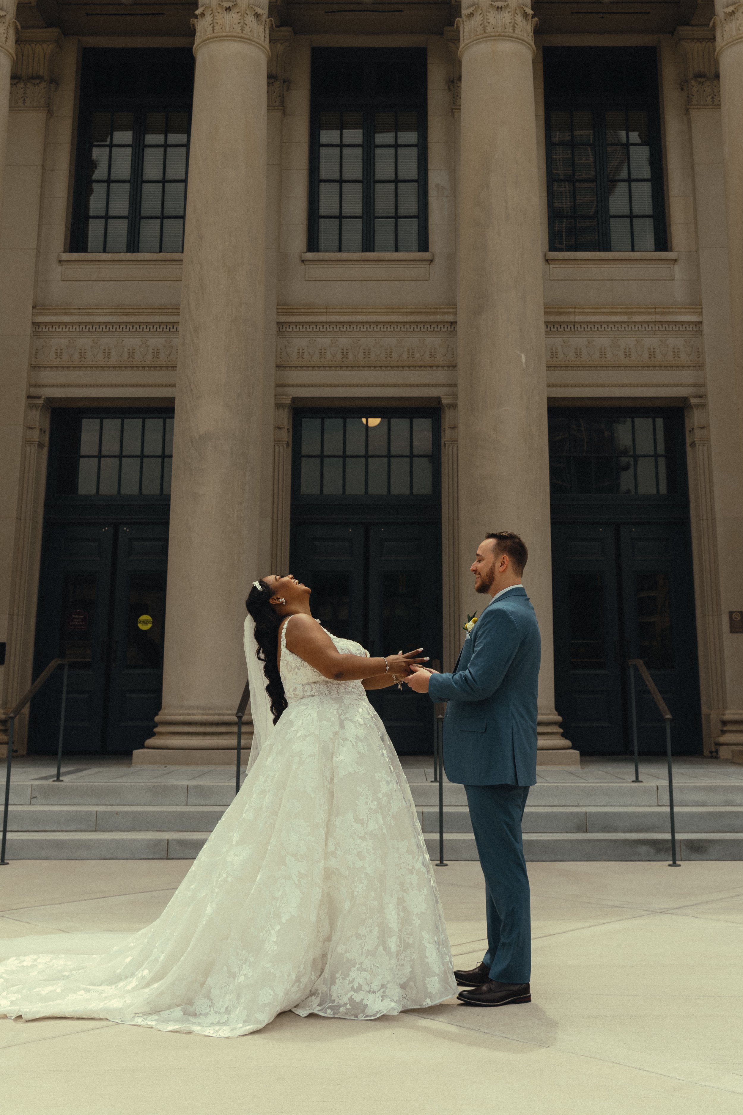 A bride and groom holding hands and looking at each other in front of a neoclassical building with large columns and steps.