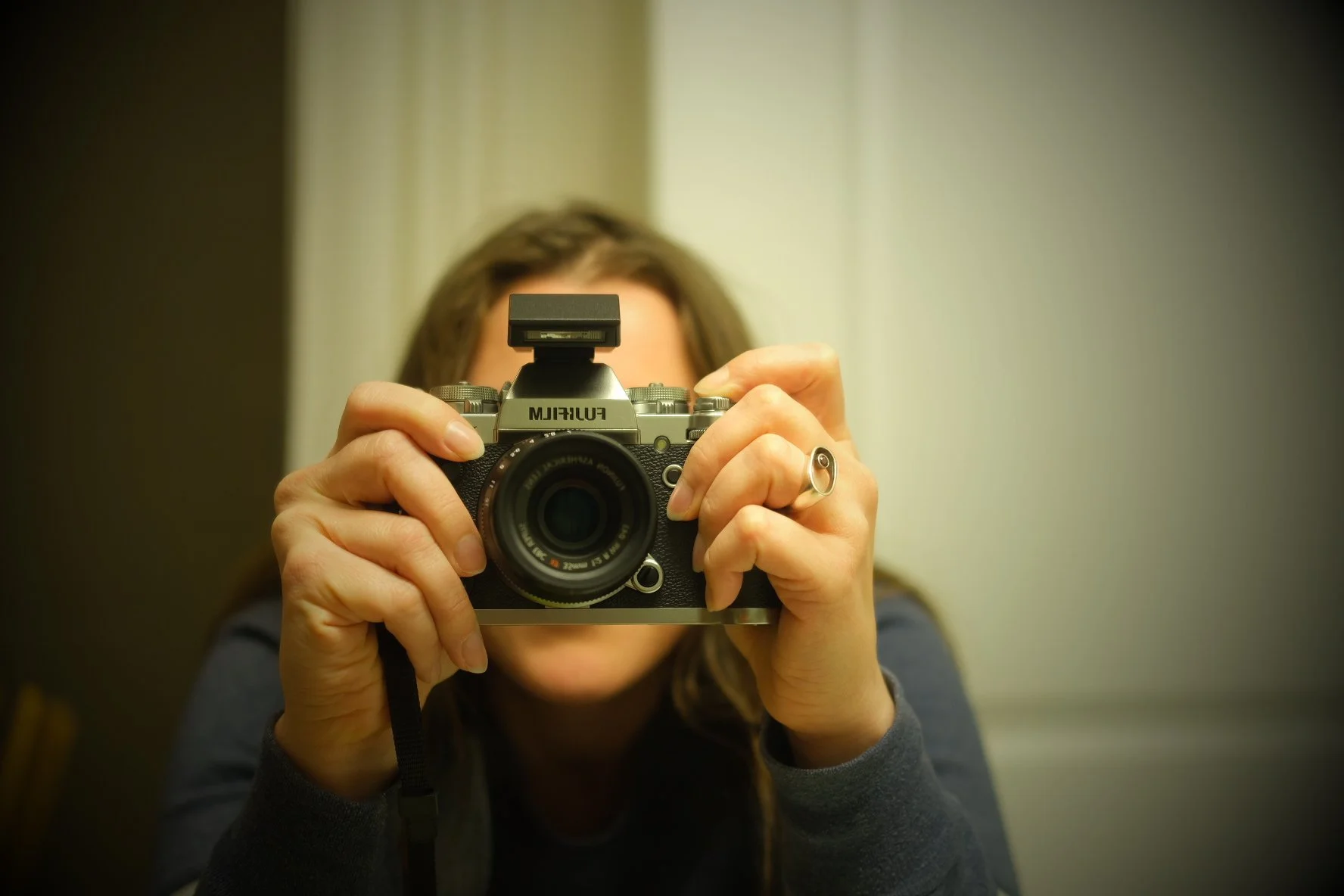 A person holding a vintage film camera and taking a self-portrait in a mirror.