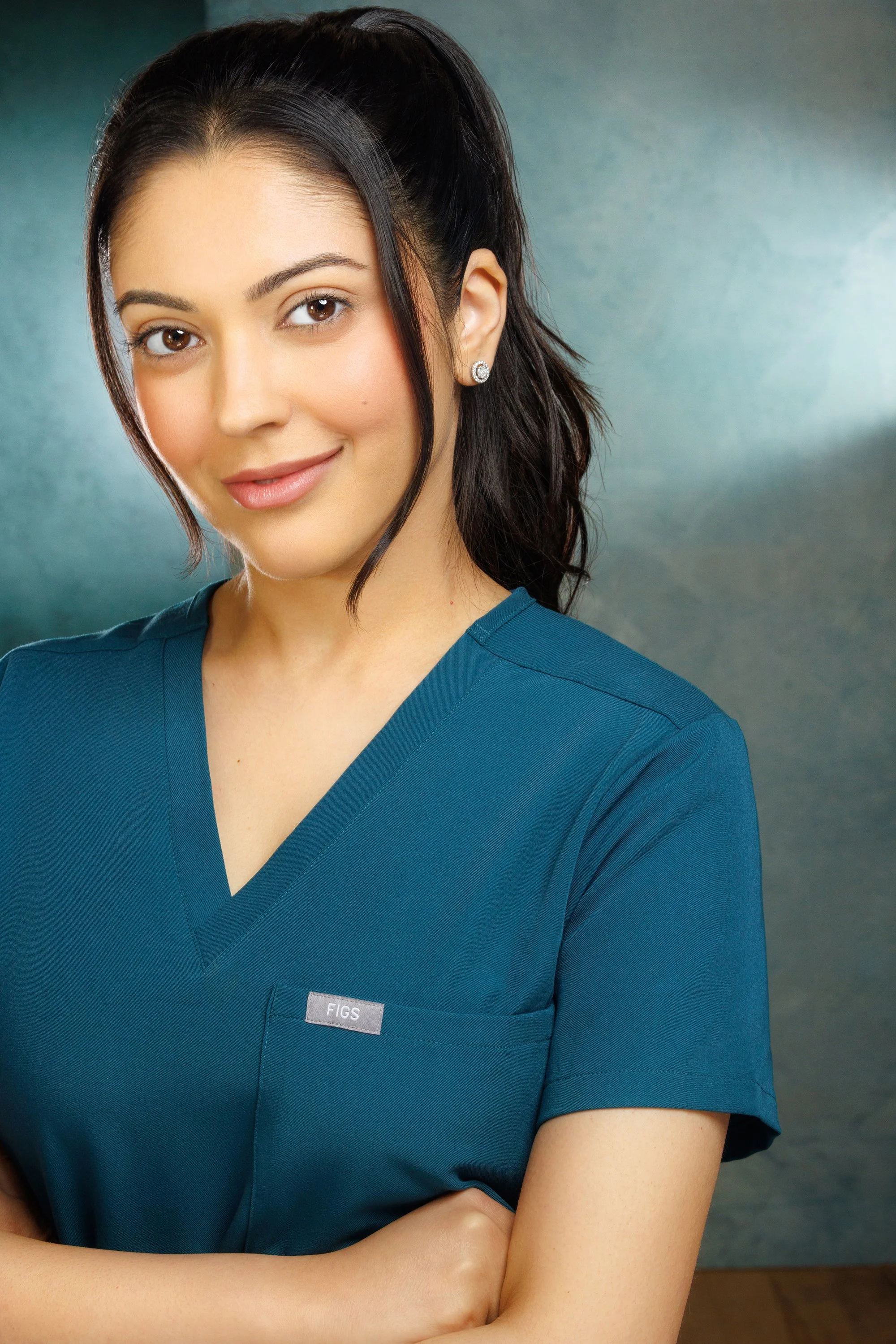 Close-up of a woman wearing a blue medical scrub with a name tag that reads 'FIGS,' smiling and looking at the camera.