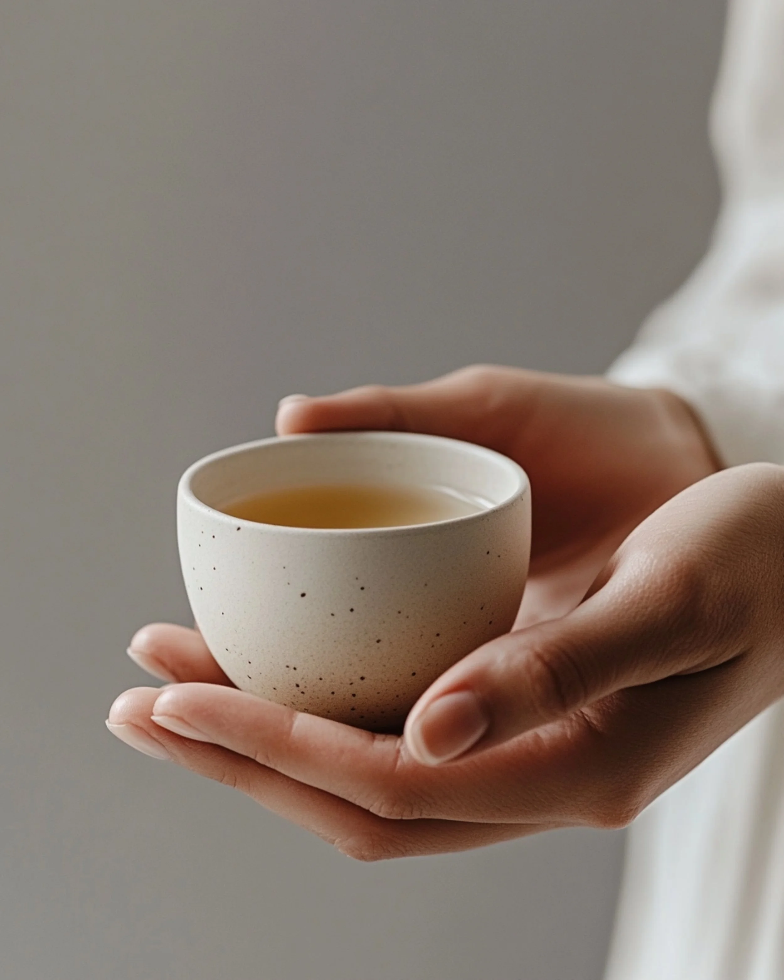 Close-up of a person's hand holding a white ceramic cup filled with tea or coffee.