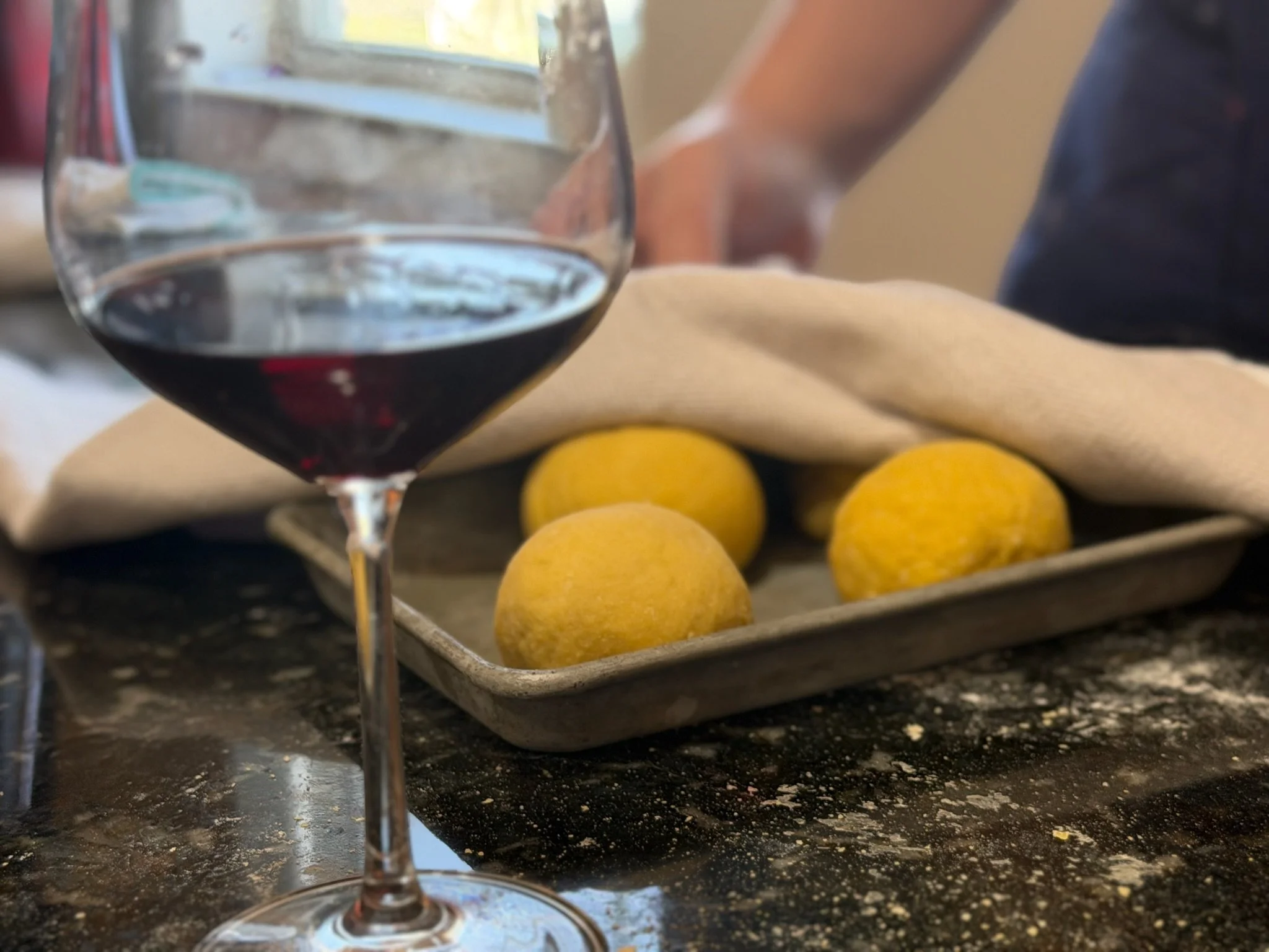 A glass of red wine on a dark, speckled kitchen countertop with lemons, a cloth, and a tray of French fries in the background at a Private Chef Lora Plauche private cooking class event.