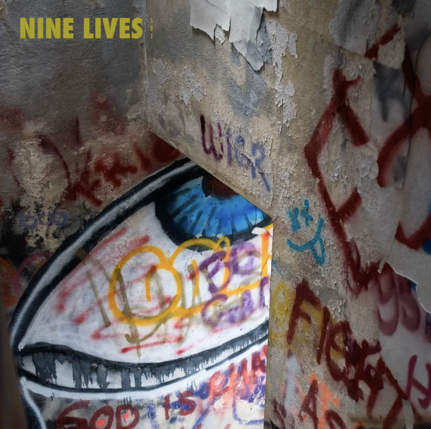 Close-up of a graffiti-covered wall with layers of peeling paint, spray-painted tags, and a painted eye with a blue iris, surrounded by colorful graffiti and markings.