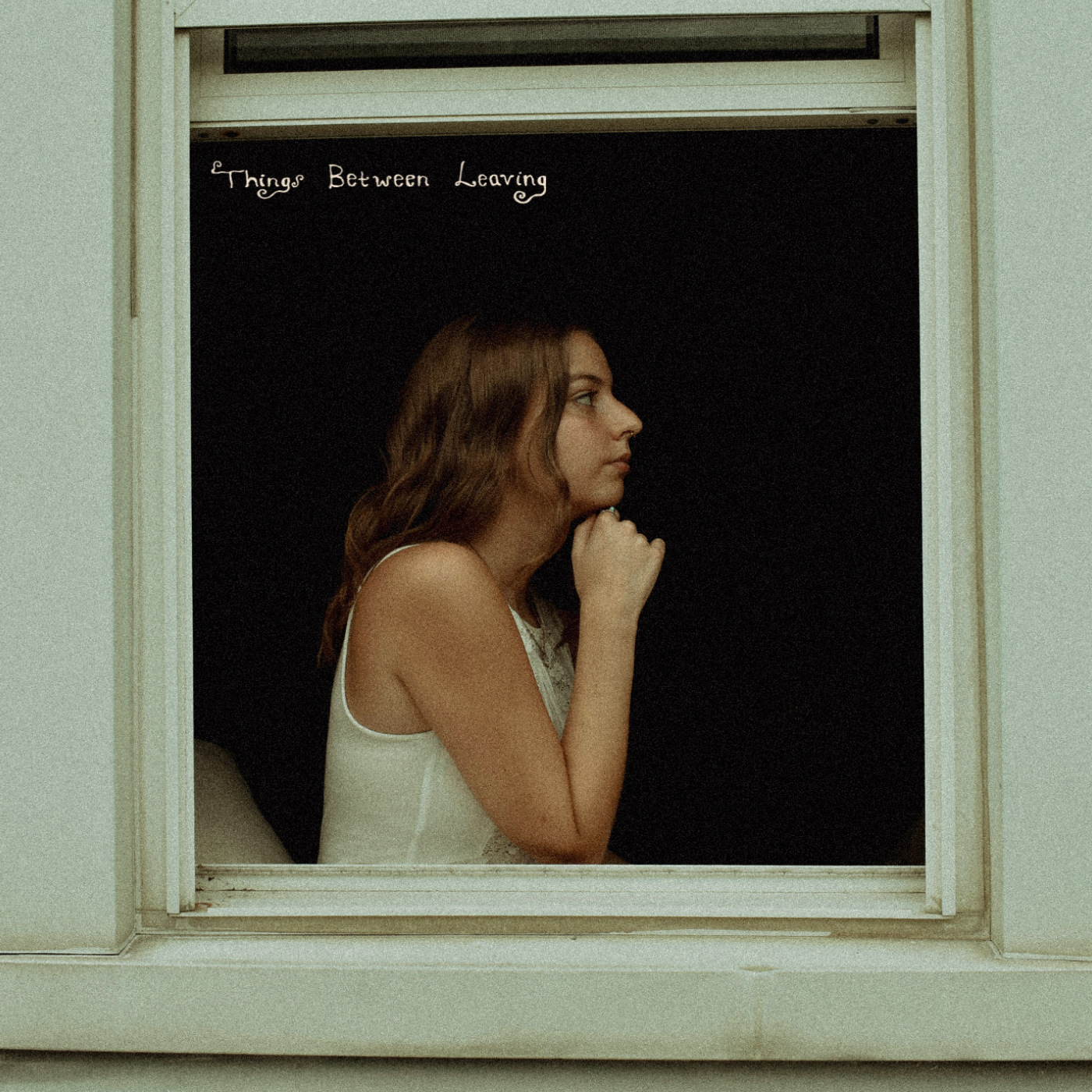 A woman with reddish-brown hair sitting in a window, looking to the right with her right hand resting under her chin. She is wearing a sleeveless top. Above her, a blackboard reads "Things Between Leaving."