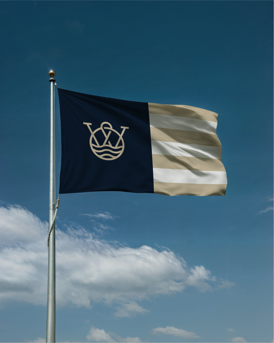 Flag with a navy blue vertical stripe on the left, featuring a white emblem of a crown with three scepters and a water motif. The right side has horizontal cream and white stripes. The flag is waving in the wind against a blue sky with scattered clouds.