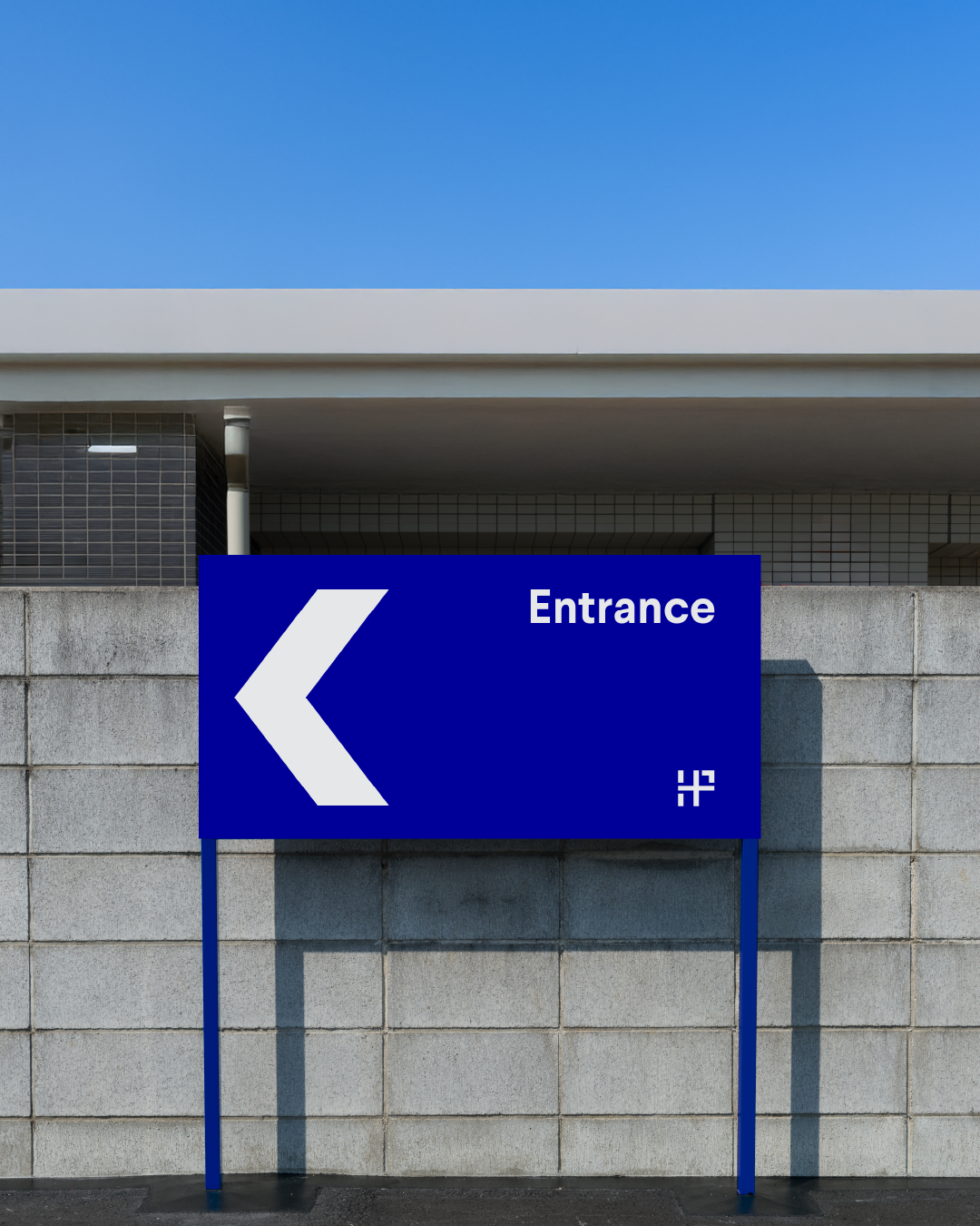Hardware Park branding: Blue directional sign with a left arrow and the word 'Entrance' mounted on a concrete wall, against a clear blue sky.
