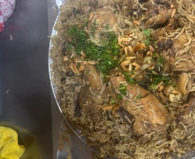A dish of cooked rice mixed with chicken, garnished with chopped herbs and toasted nuts.