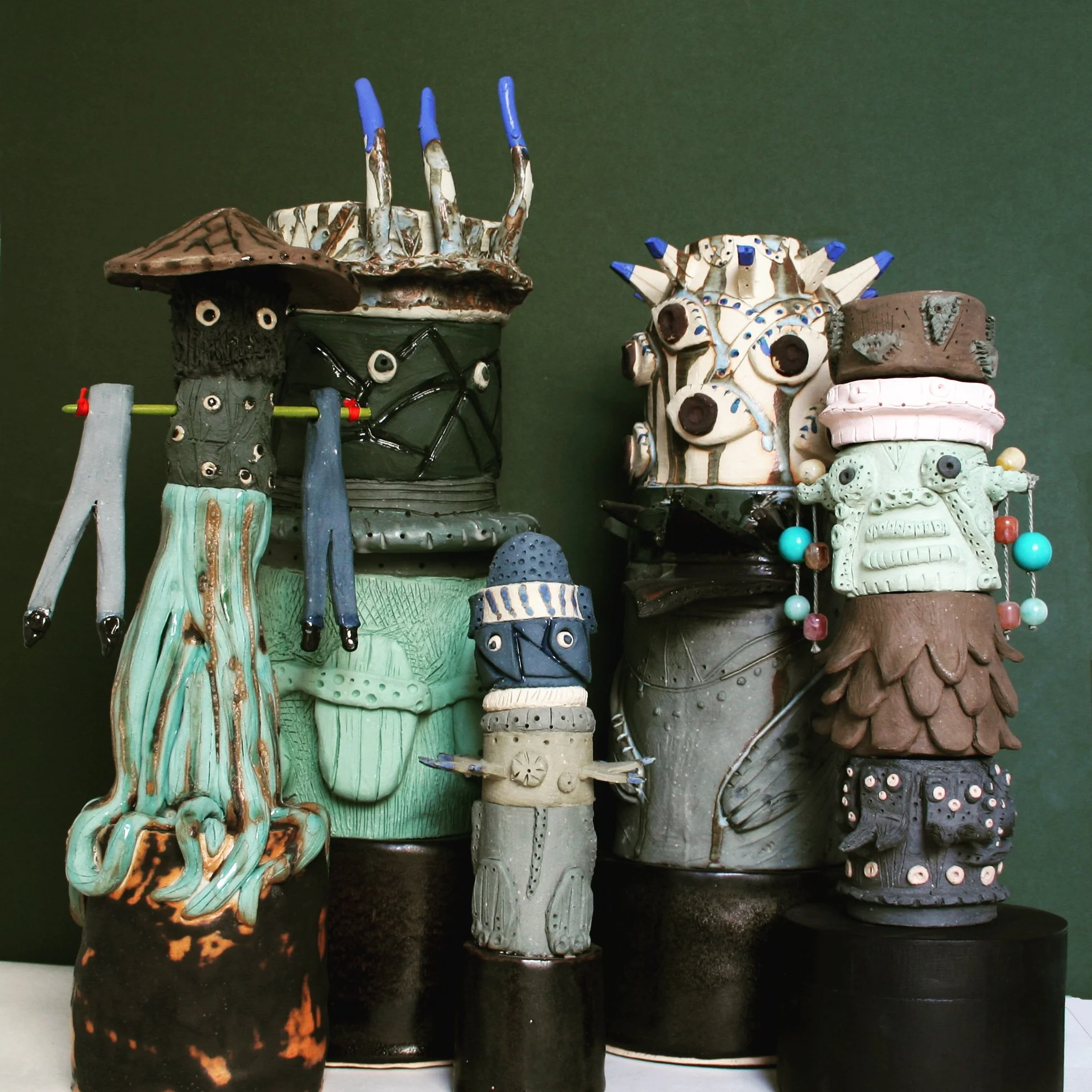 Collection of anthropomorphic ceramic sculptures resembling mythical creatures with detailed features, spikes, and vibrant colors, displayed against a dark background.