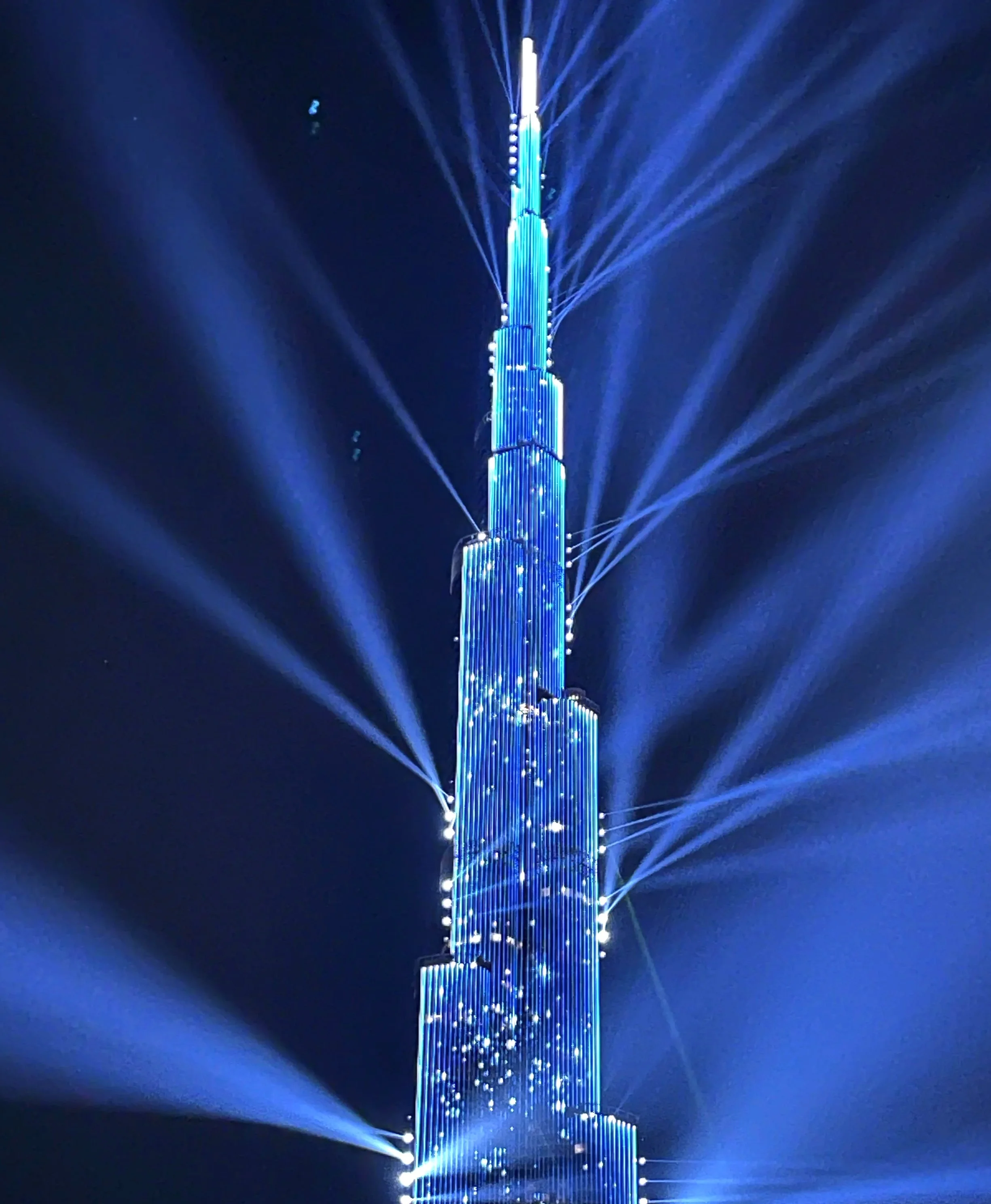 Nighttime view of the Burj Khalifa illuminated with blue lights and surrounded by bright laser beams in Dubai.
