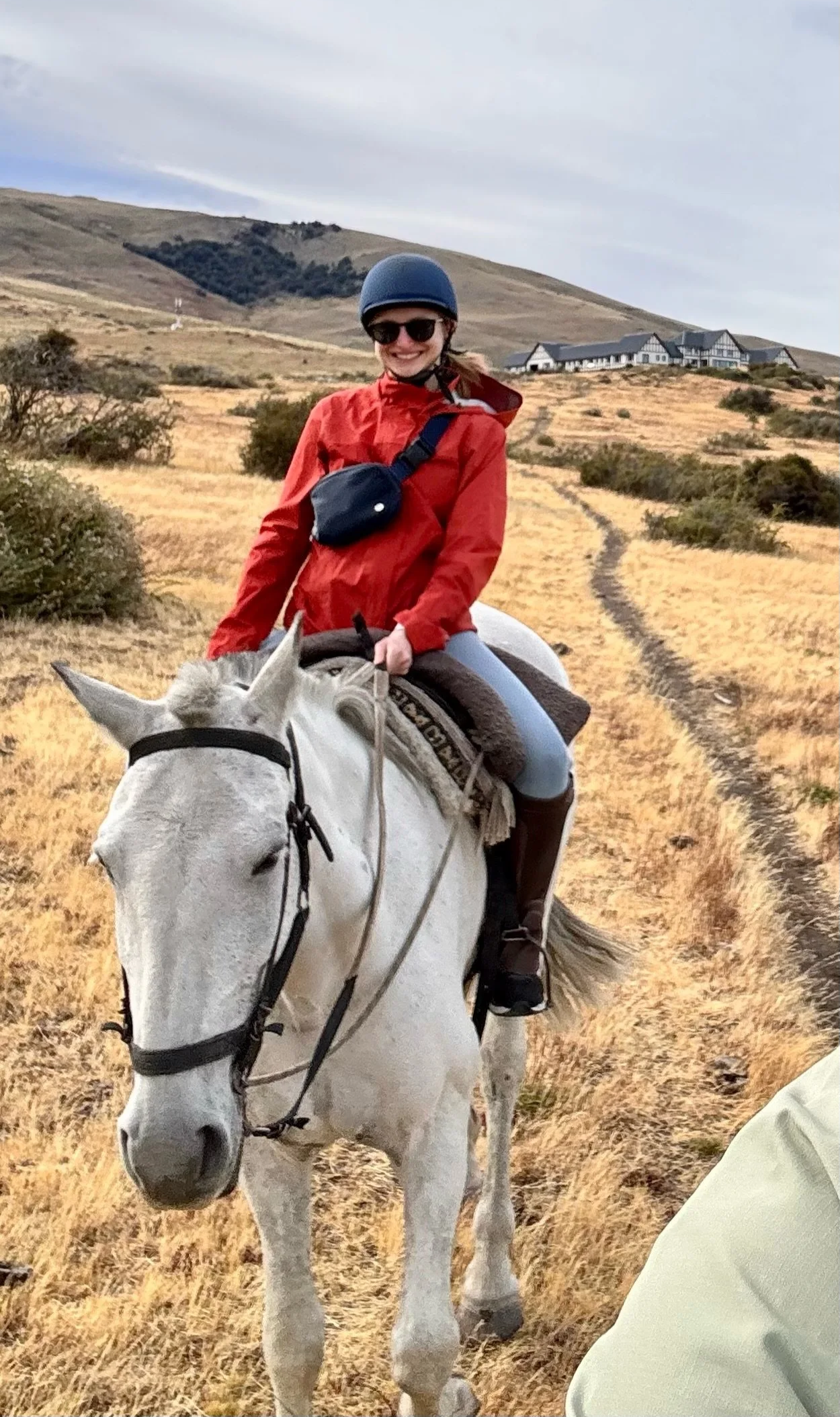 Woman in an orange raincoat riding a white horse in a dramatic setting in Patagonia.