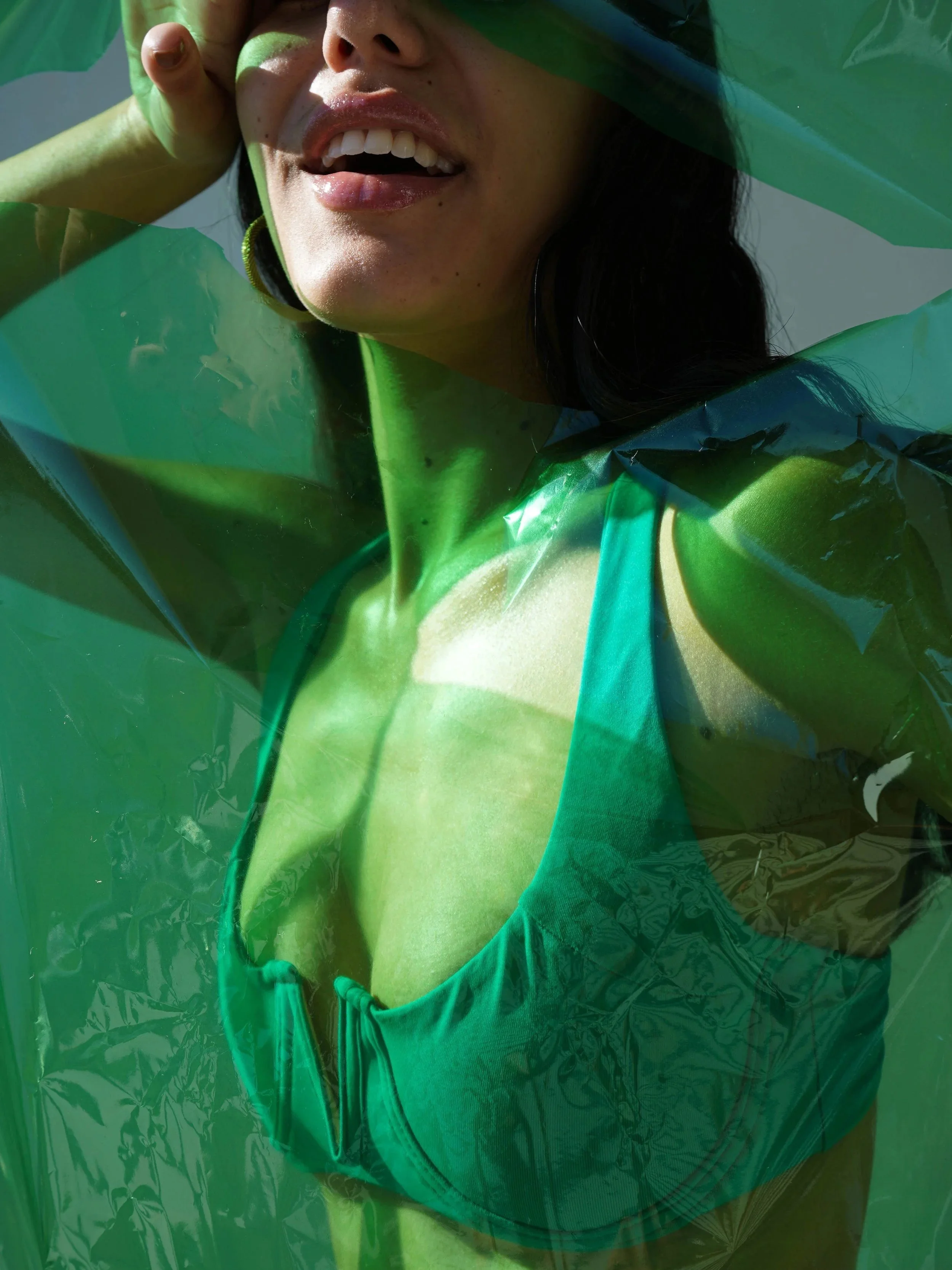 A woman wearing a bright green top and a green plastic bag over her shoulders, smiling with her mouth open.