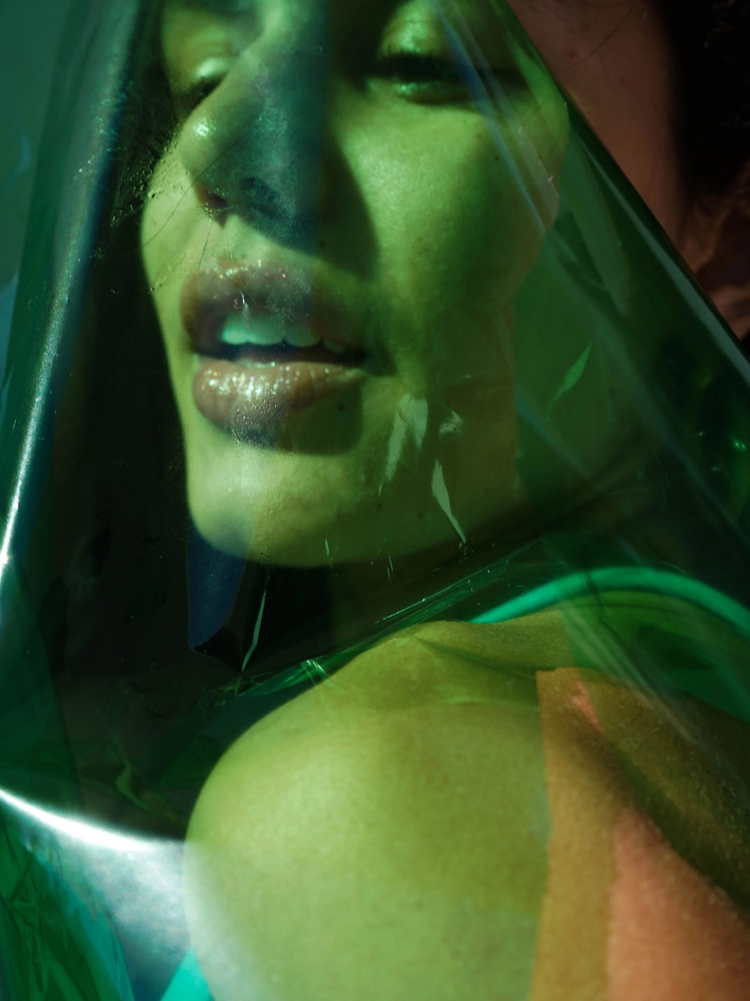 A woman's face behind green-tinted plastic, with her mouth open and tongue slightly sticking out.