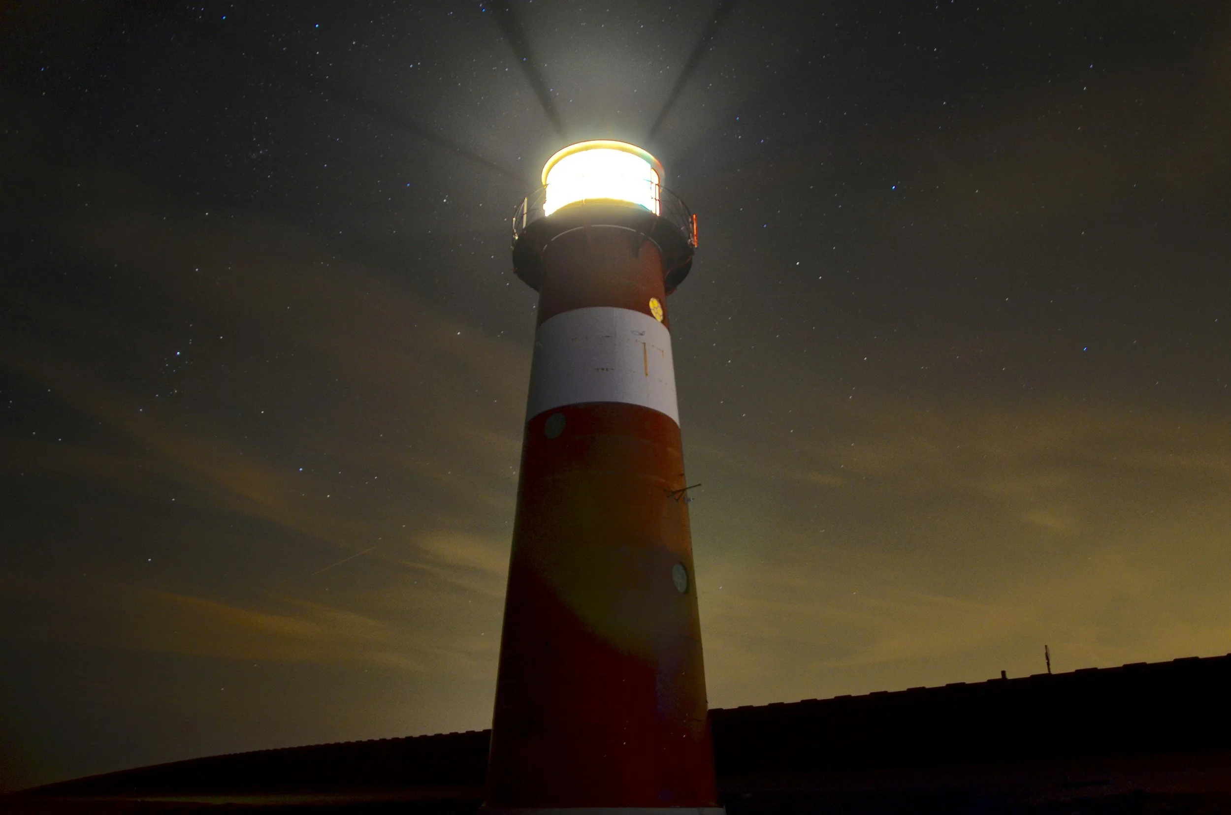 Nighttime photo of a lighthouse with the light on, standing against a starry sky.