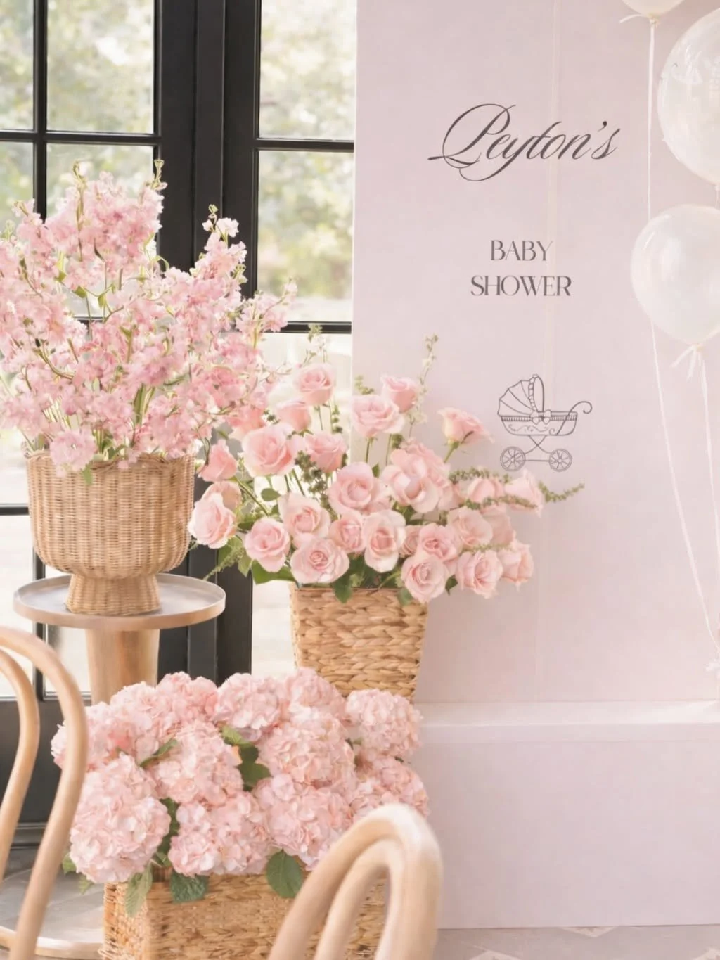 Pink floral arrangements including roses, hydrangeas, and cherry blossoms in wicker baskets at a baby shower with a sign that reads 'Leyton's Baby Shower' and white balloons.