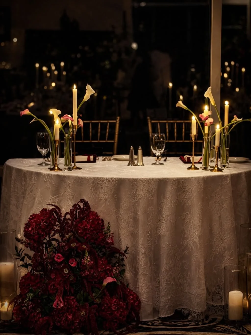 A beautifully decorated table set with candles, flowers, and glassware for a romantic or formal dinner, with dark background and warm lighting.